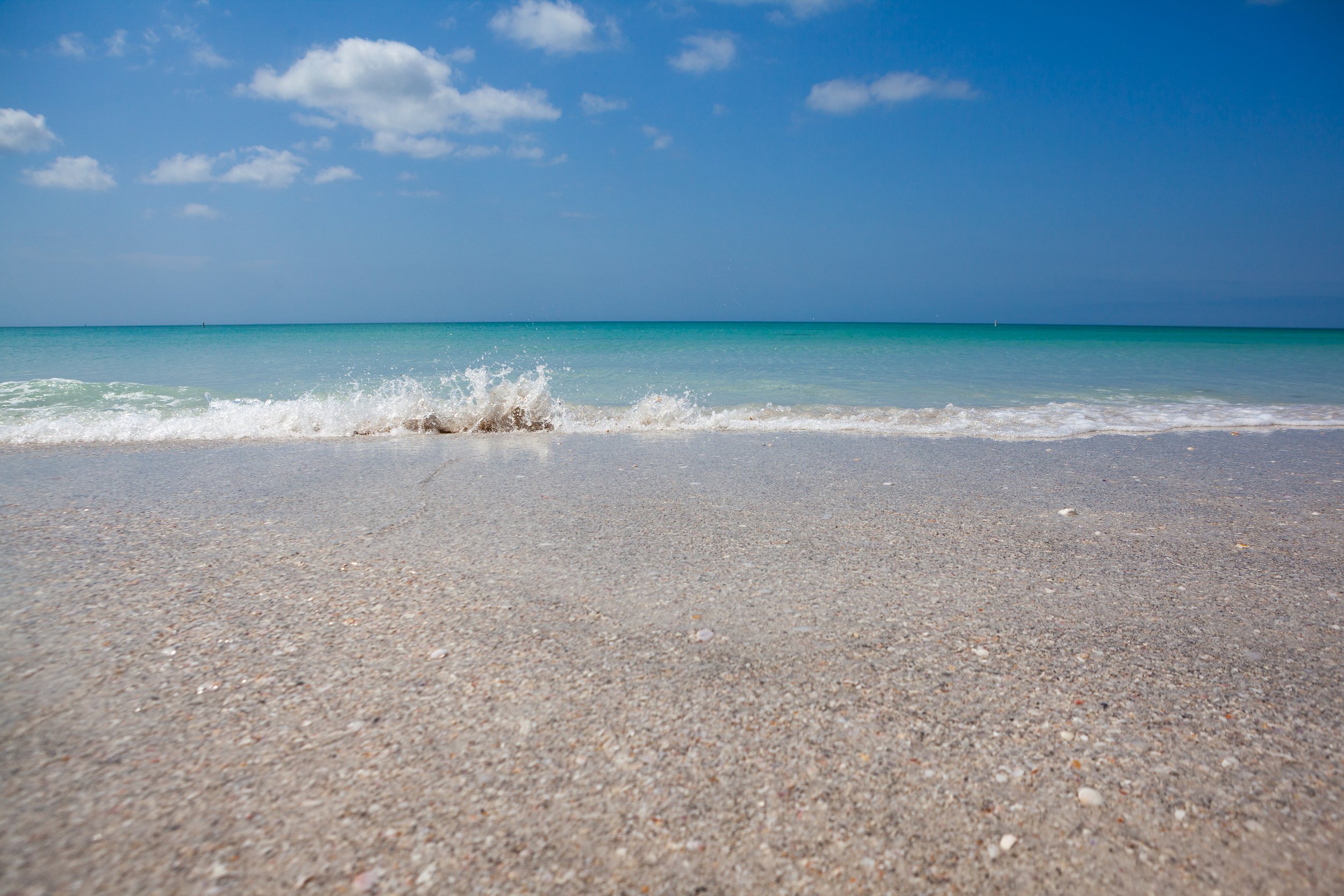 View of a sandy beach with gentle waves and a clear blue sky.