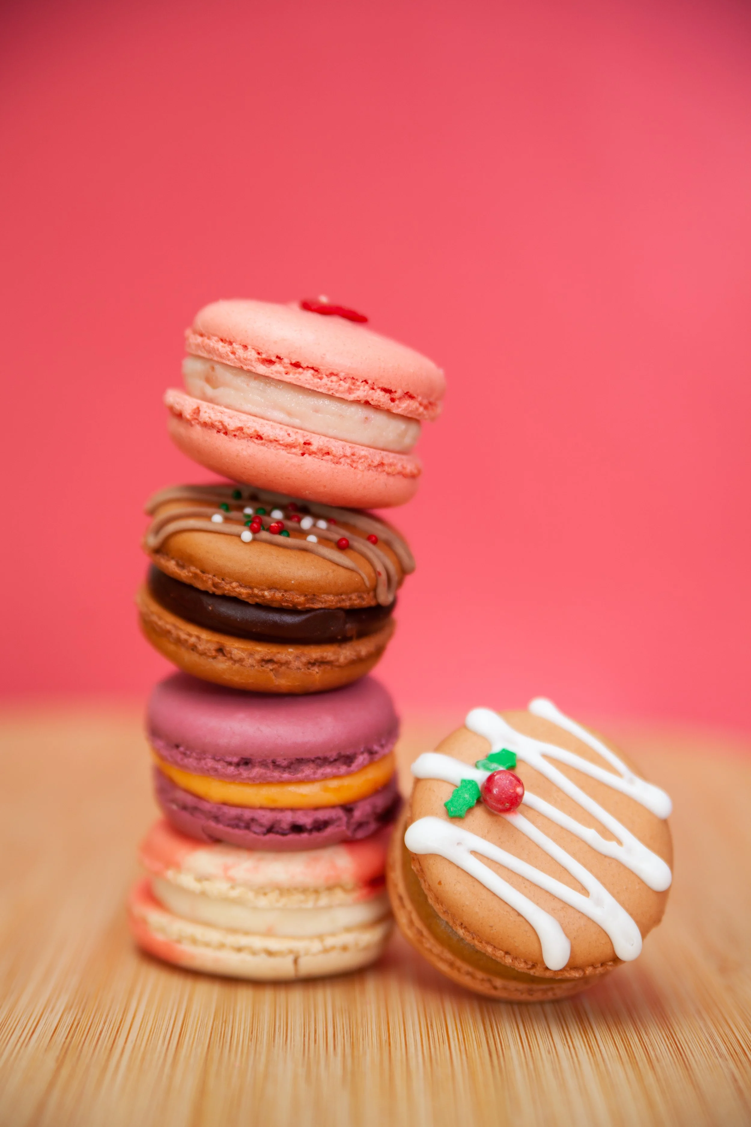 Stack of colorful macarons on a wooden surface with a pink background.