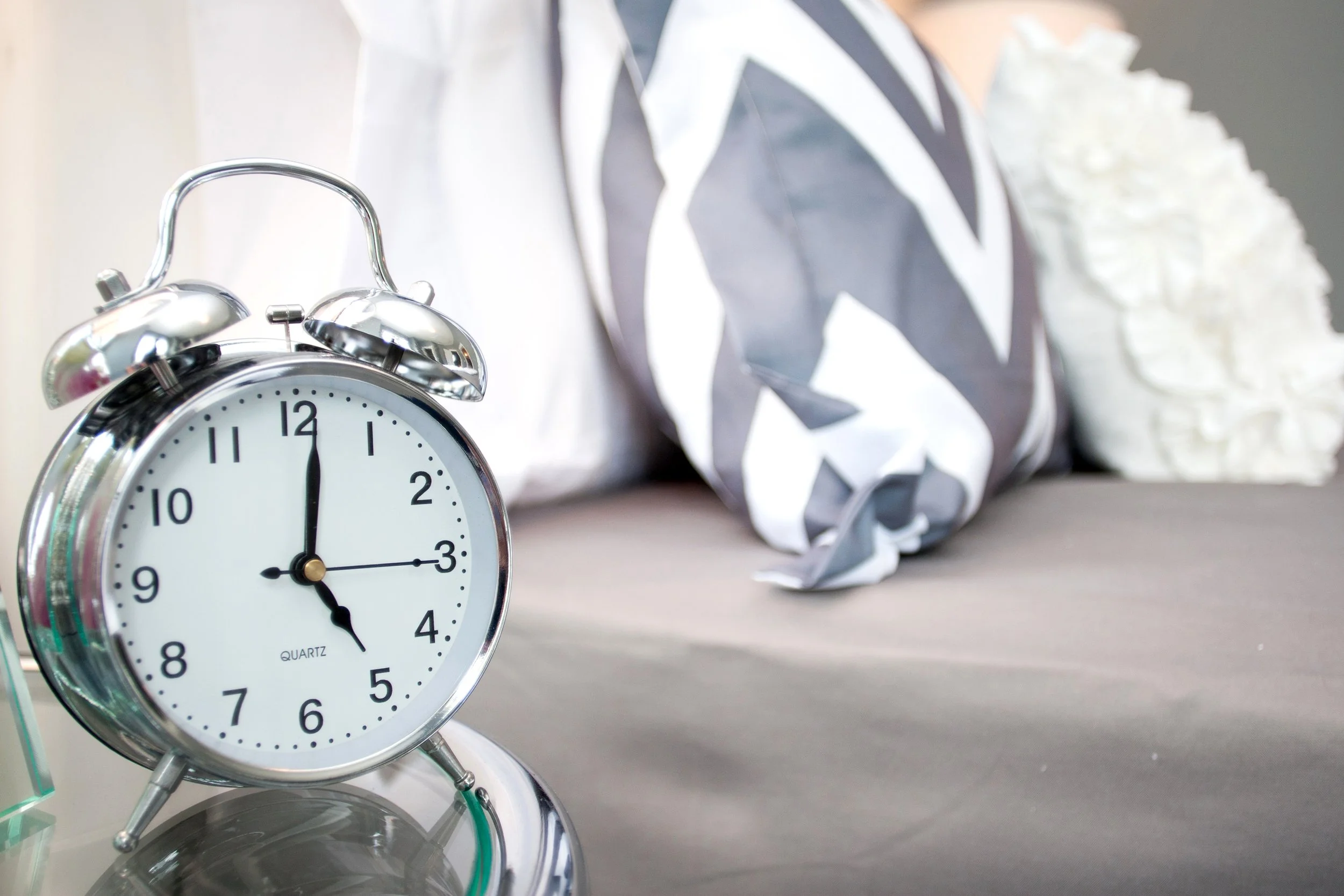 Silver alarm clock showing 12:00 on a bedside table with crumpled tissue paper in the background.