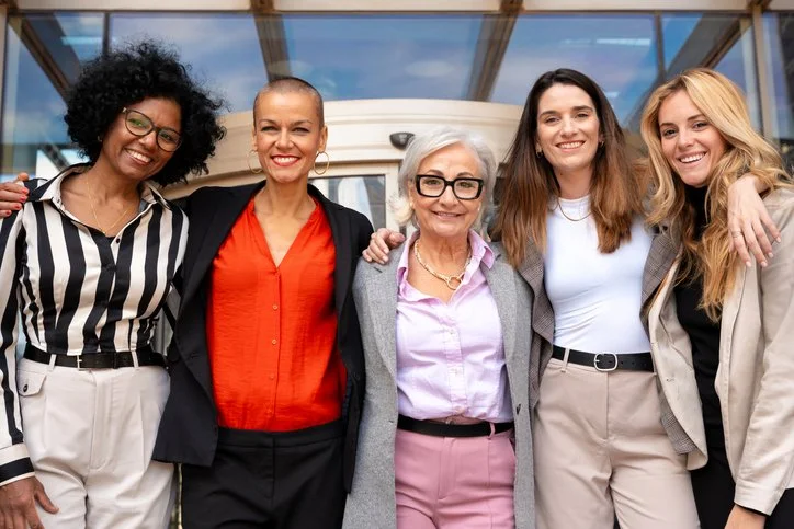 Five women standing together in front of an airplane, smiling at the camera.
