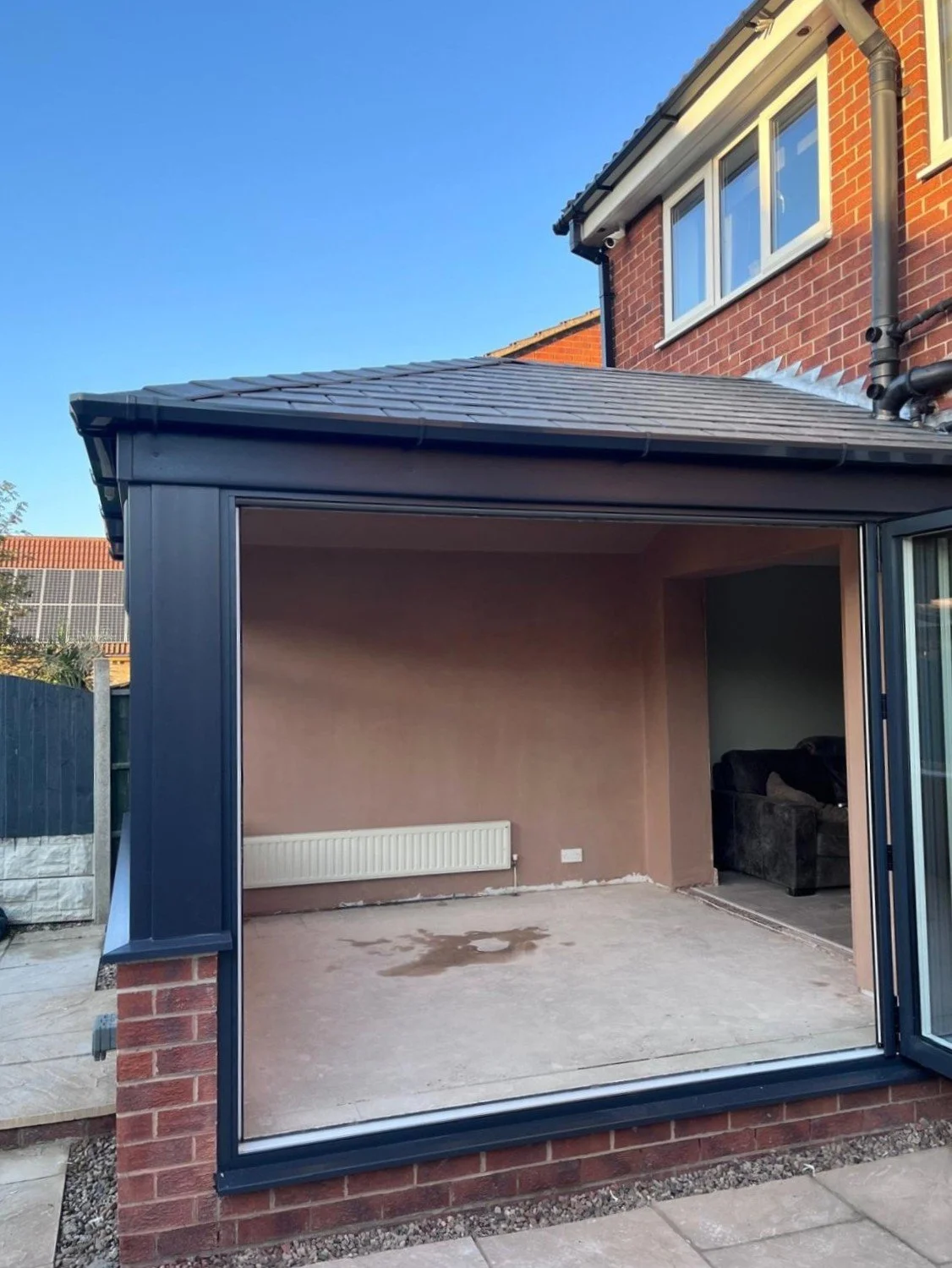 Unfinished outdoor patio space with brick wall, heater, and part of a house with a window, under a blue sky.