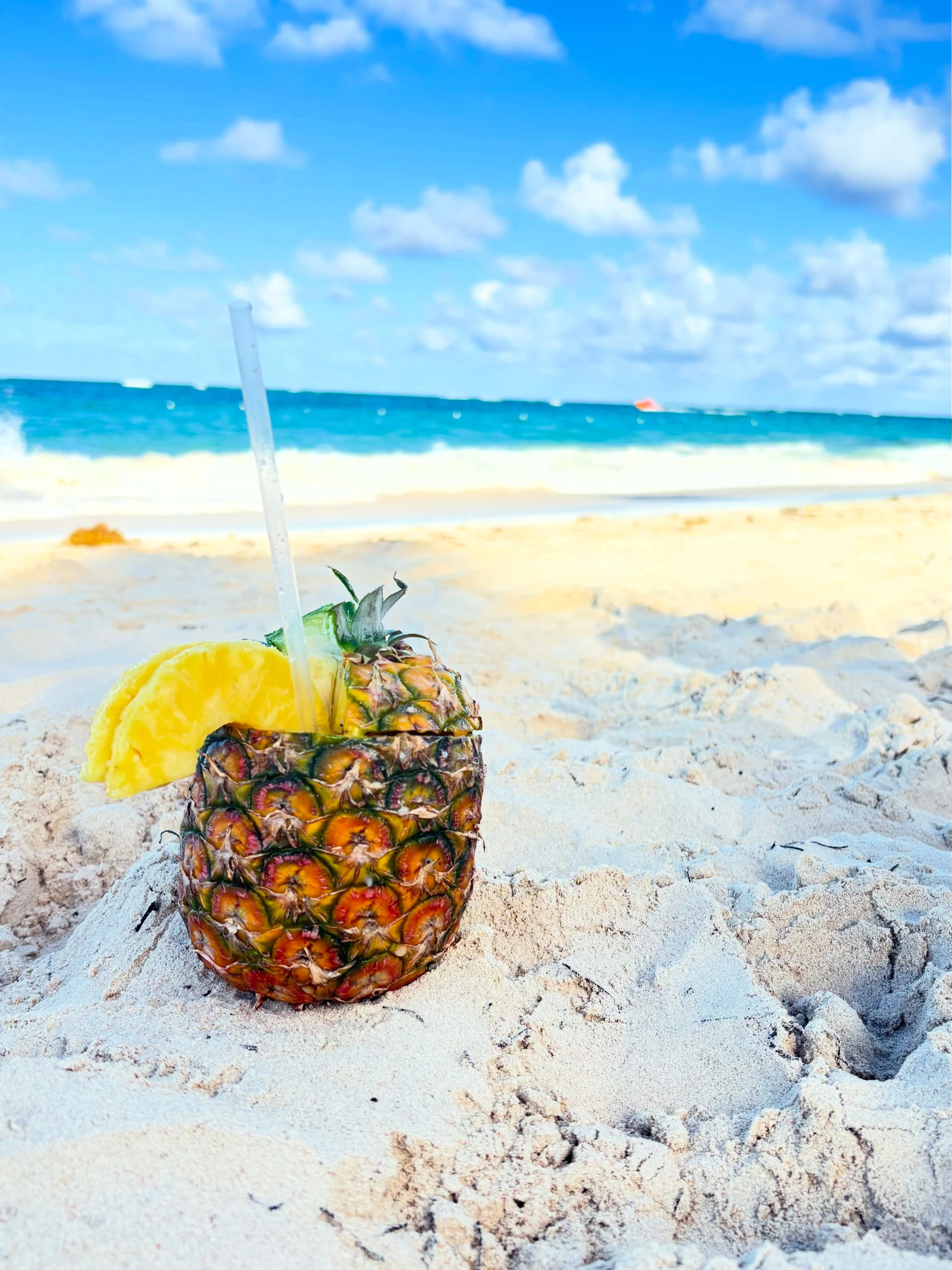 Piña con rodaja de piña y pajilla en la playa.