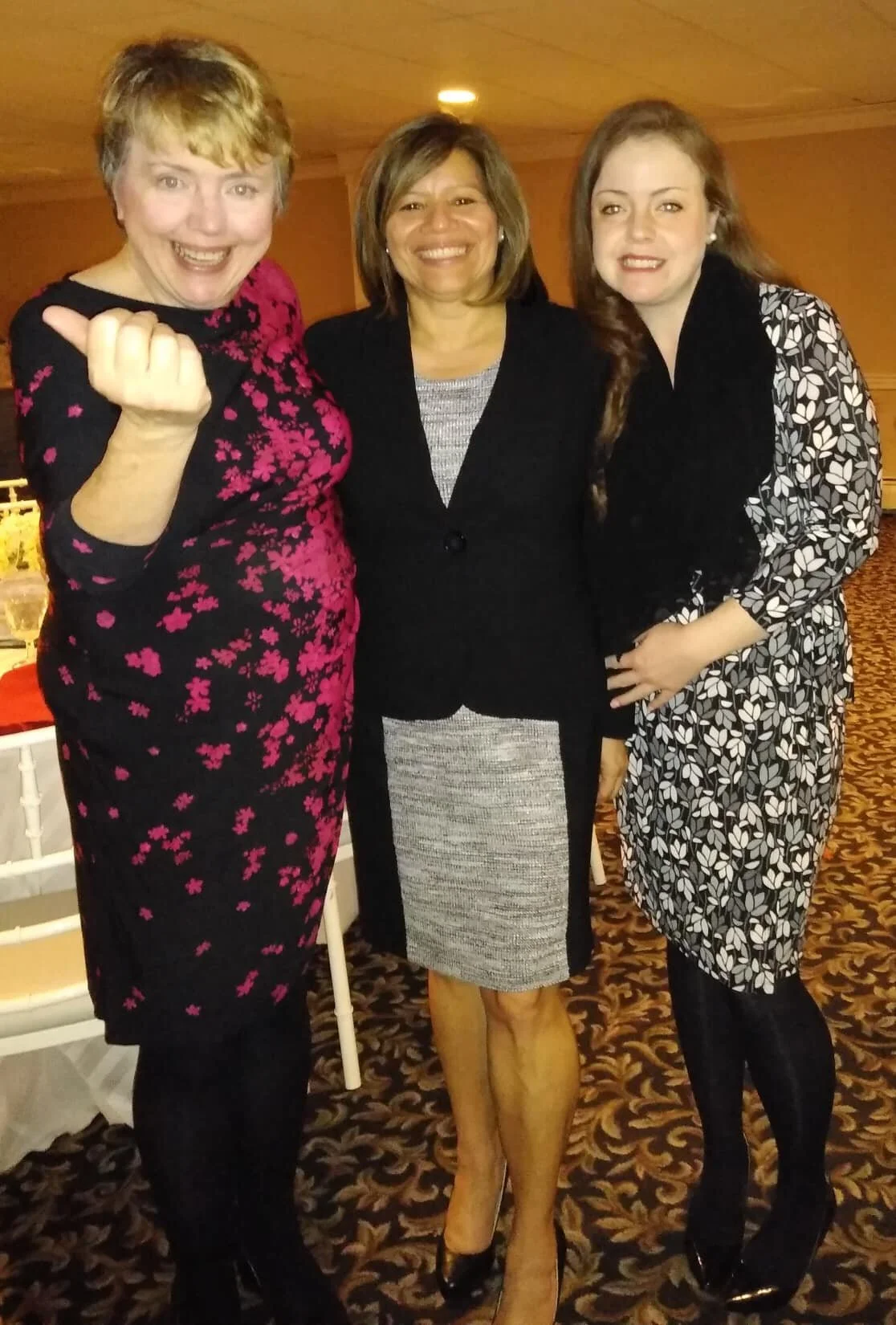 Three women standing close together indoors, smiling at the camera.