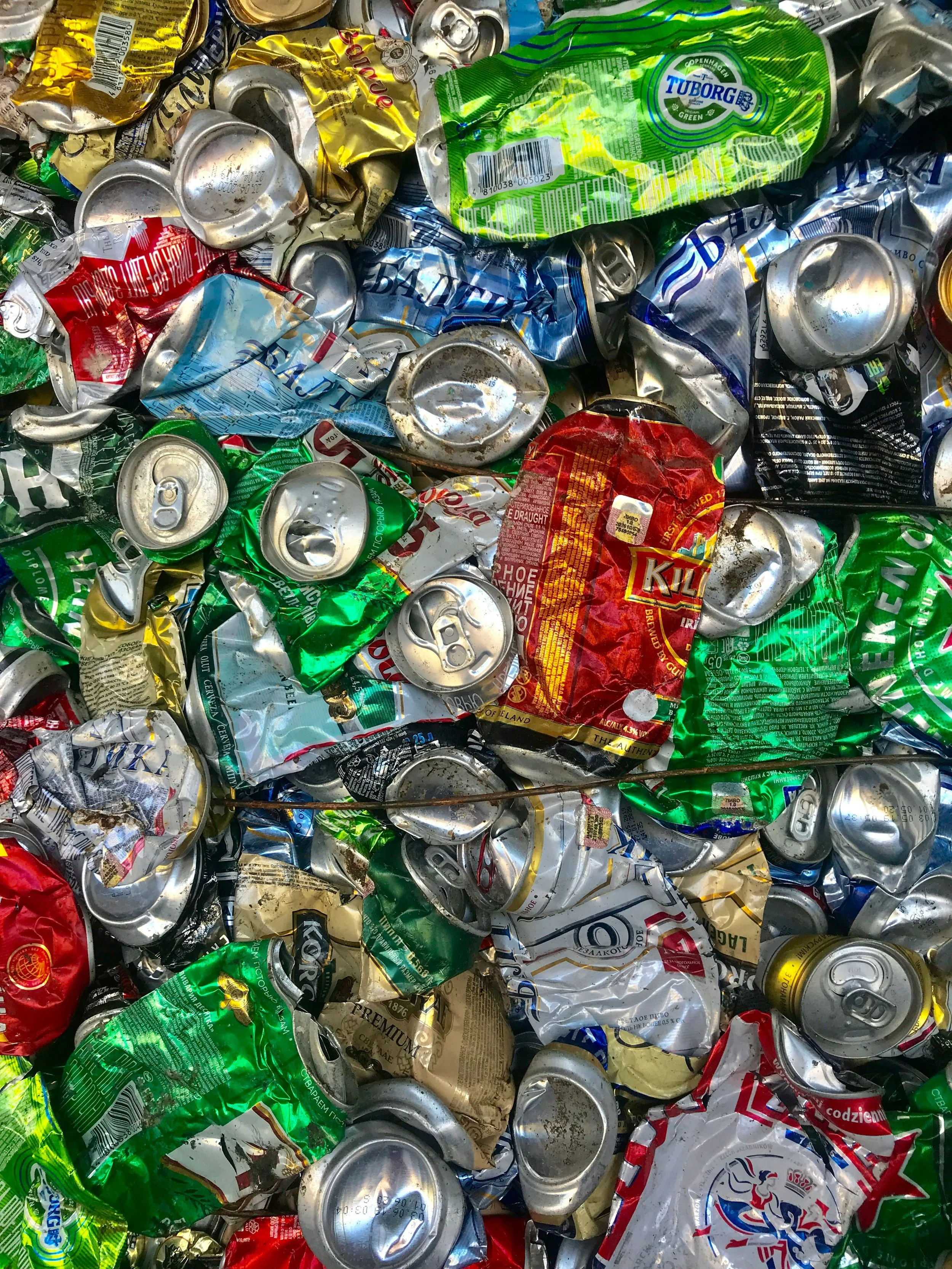 A pile of crushed aluminum cans of various colors including green, red, blue, yellow, and gold, with some cans' tops and pull-tabs visible.
