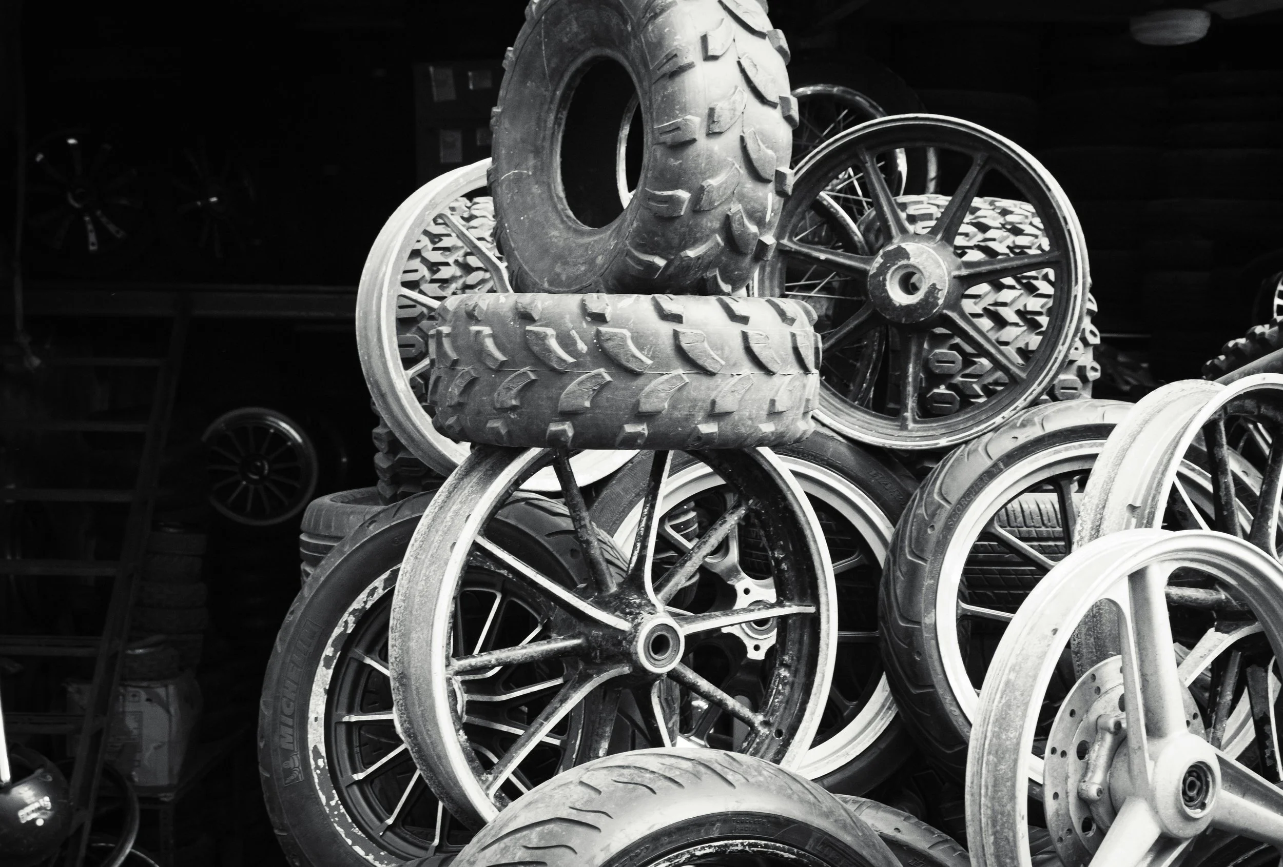 Stack of various discarded vehicle tires and wheels, some stacked on top of each other in black and white.
