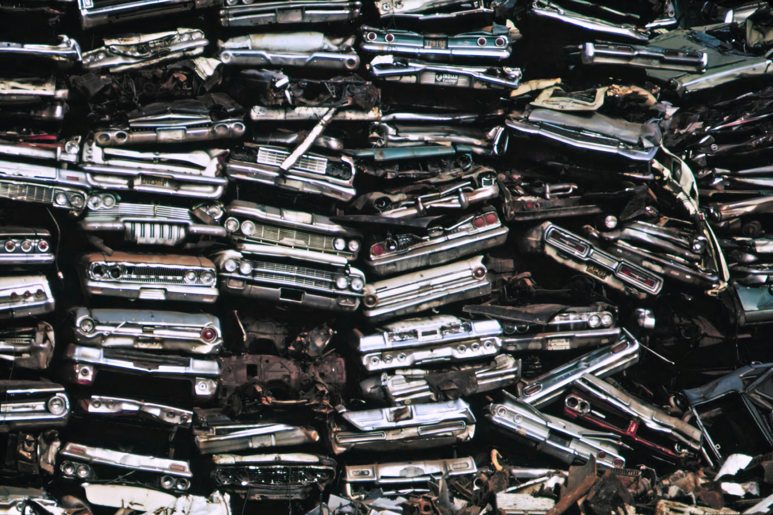 Pile of vintage car front ends, stacked chaotically, with chrome bumpers, grills, and lights visible.