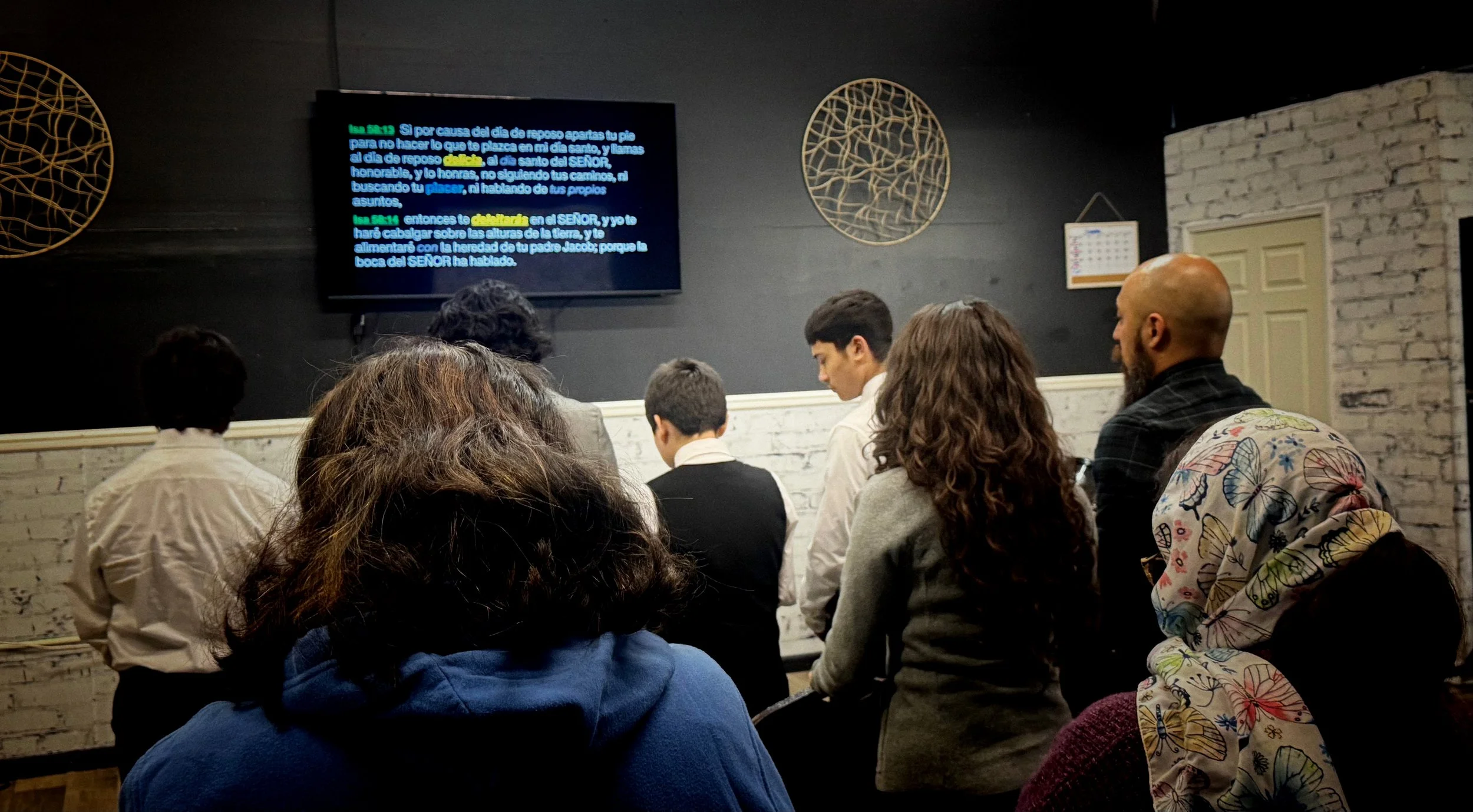 People seated in a room watching a presentation on a wall-mounted screen.