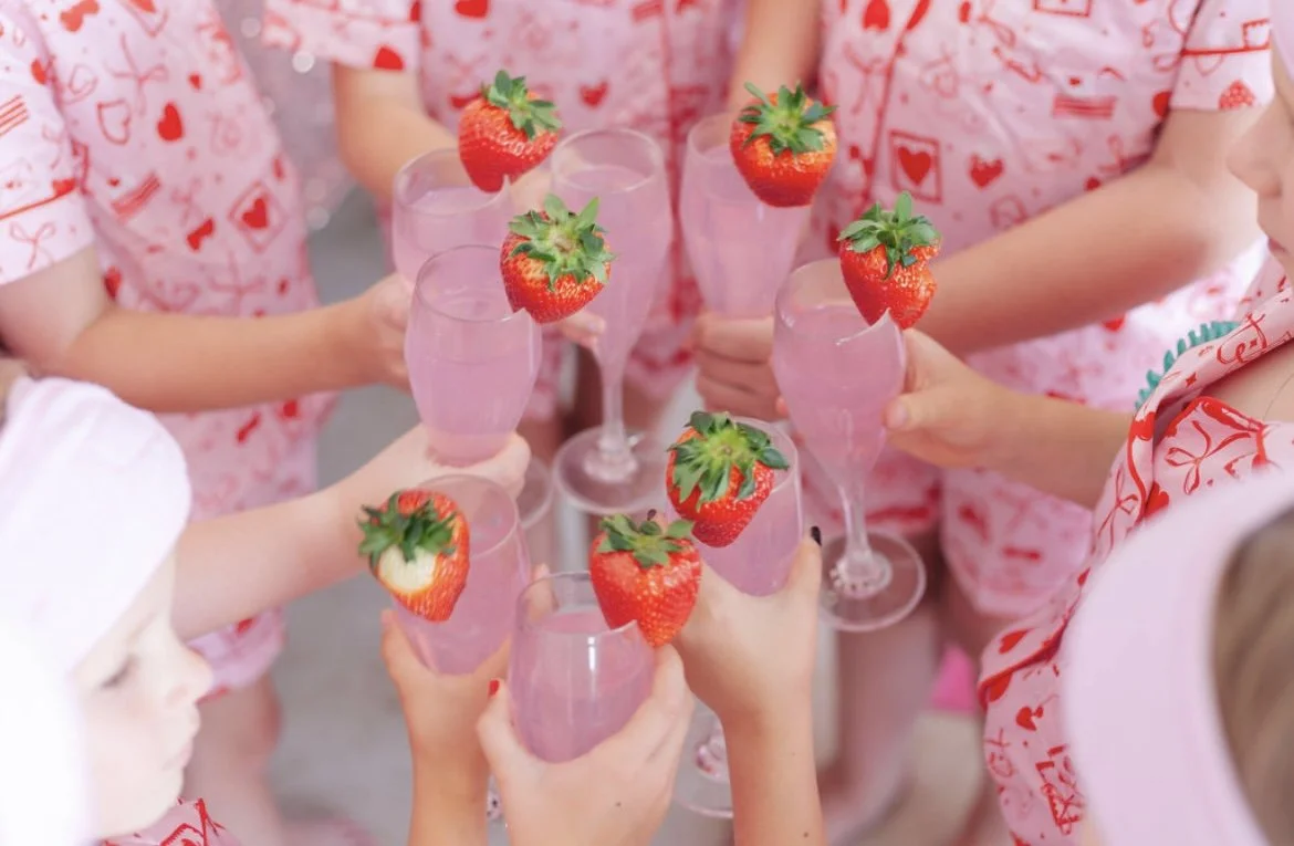 Children in matching pajamas holding pink drinks topped with strawberries in a toast.