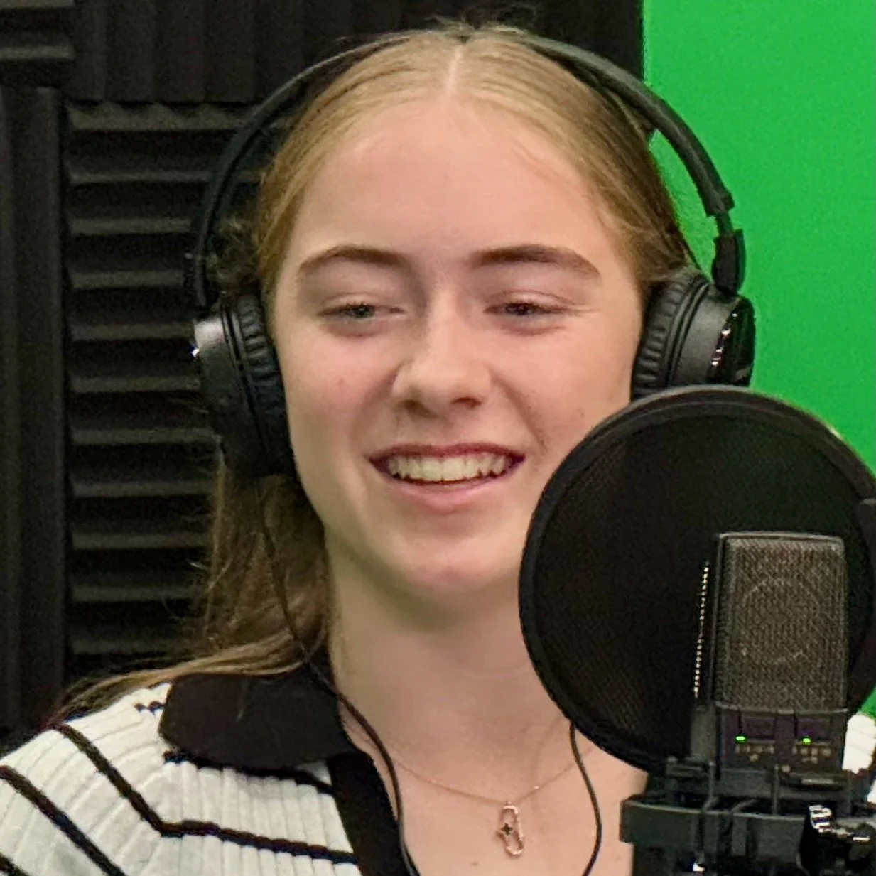 Teen Exec founder Natalya Lucas wearing headphones and smiling, speaking into a professional microphone in a studio recording an episode for the Teen Exec Podcast.