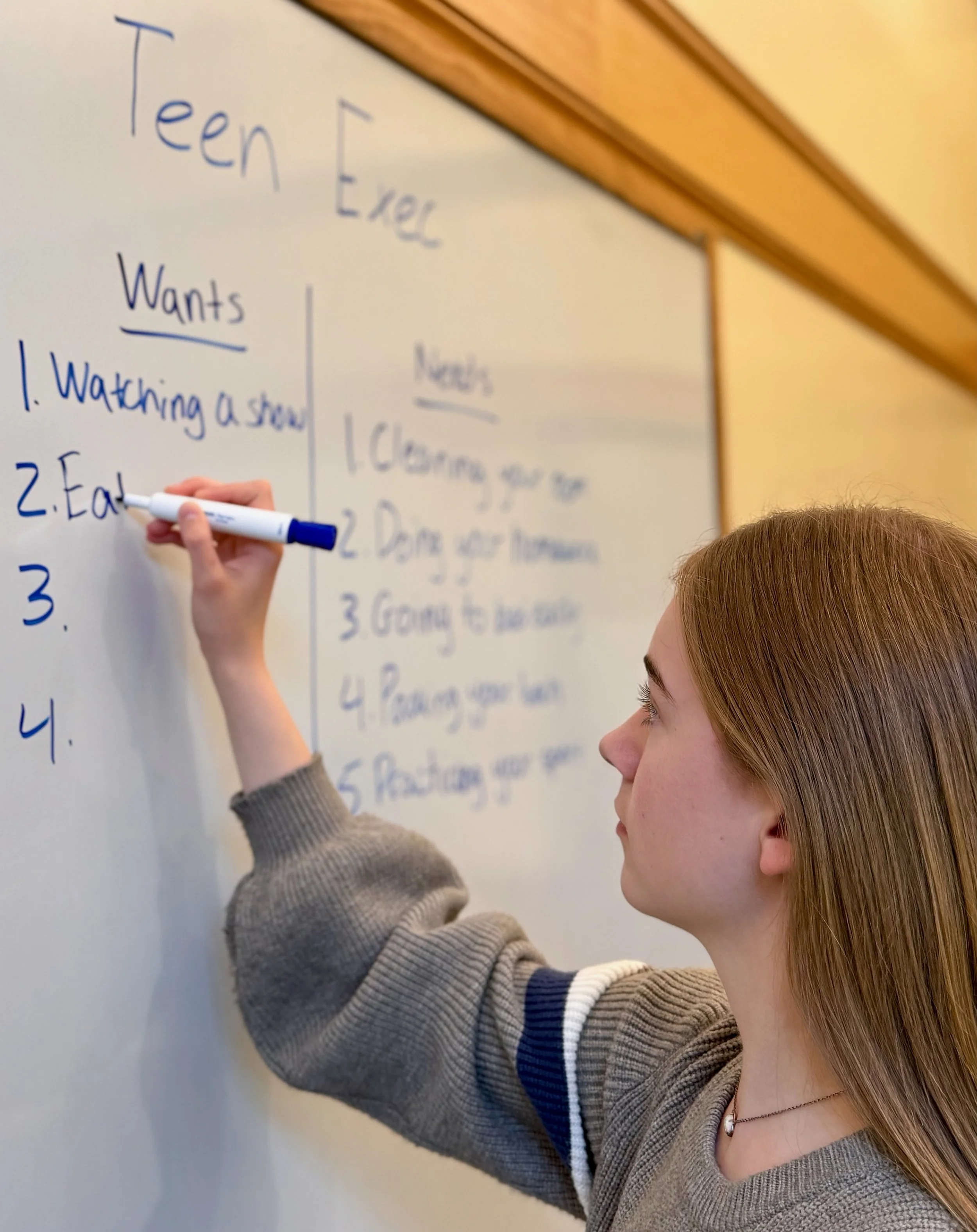 Teen Exec founder Natalya Lucas is writing on a whiteboard during a workshop with students on time management. The whiteboard has writing about 'teen' and 'wants' with a list of items underneath.