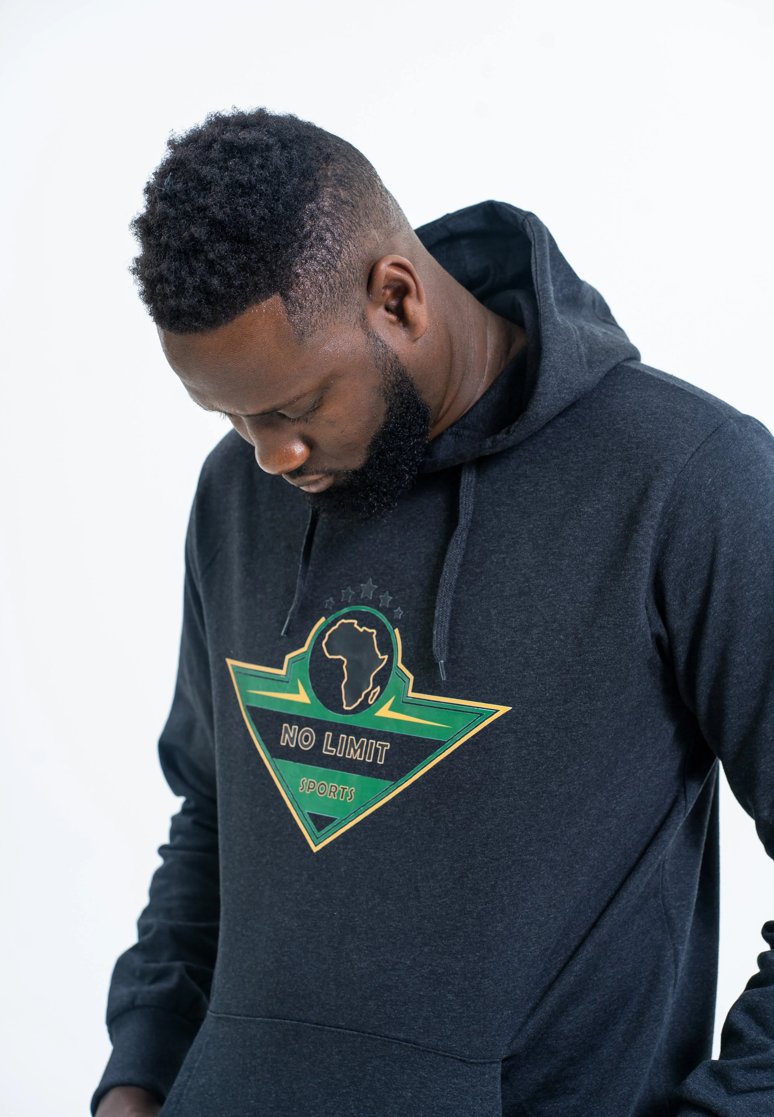 Le PDG de No Limit Sports portant un hoodie noir avec un logo vert et jaune représentant une carte de l'Afrique et le texte 'No Limit Sports', son visage est penché vers le bas, face cachée.