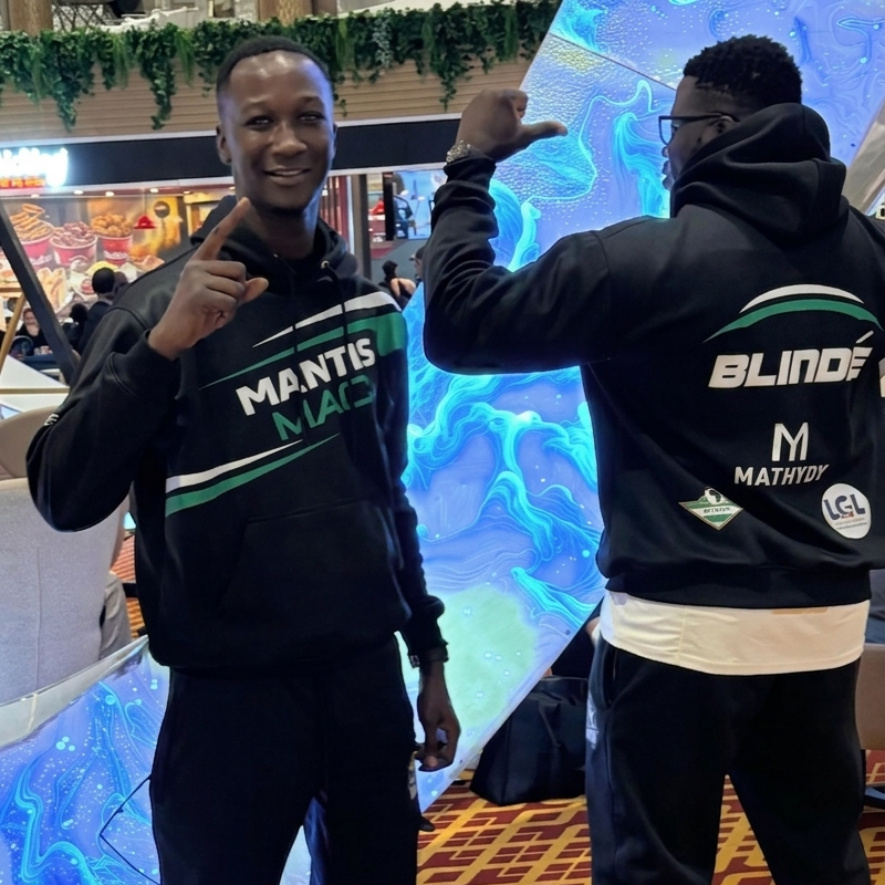 Two men posing together outside a modern glass building; one wears a black polo with the No Limit Sports logo, and the other is a professional fighter in a black PFL (Professional Fighters League) hoodie.