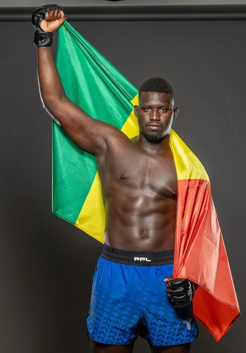 ABDOULAYE KANE portant des gants de boxe, tenant un drapeau du Sénégal sur ses épaules, regardant l'objectif avec expression sérieuse.