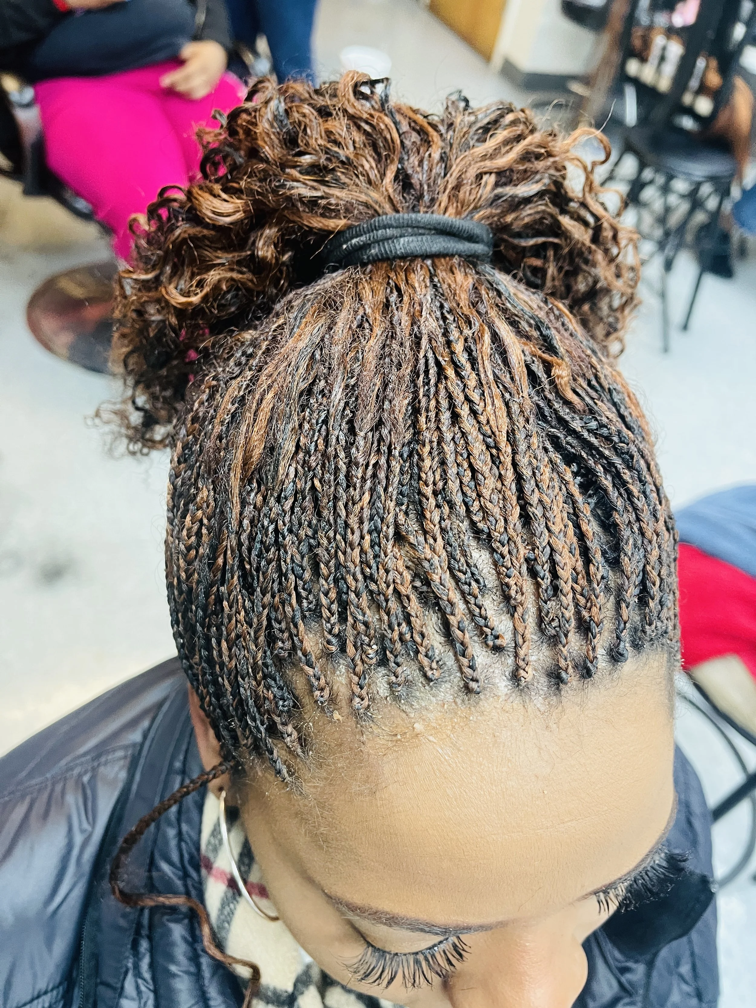 A woman with short, patterned braids and curly hair on top, wearing black clothing, in a salon or similar setting.
