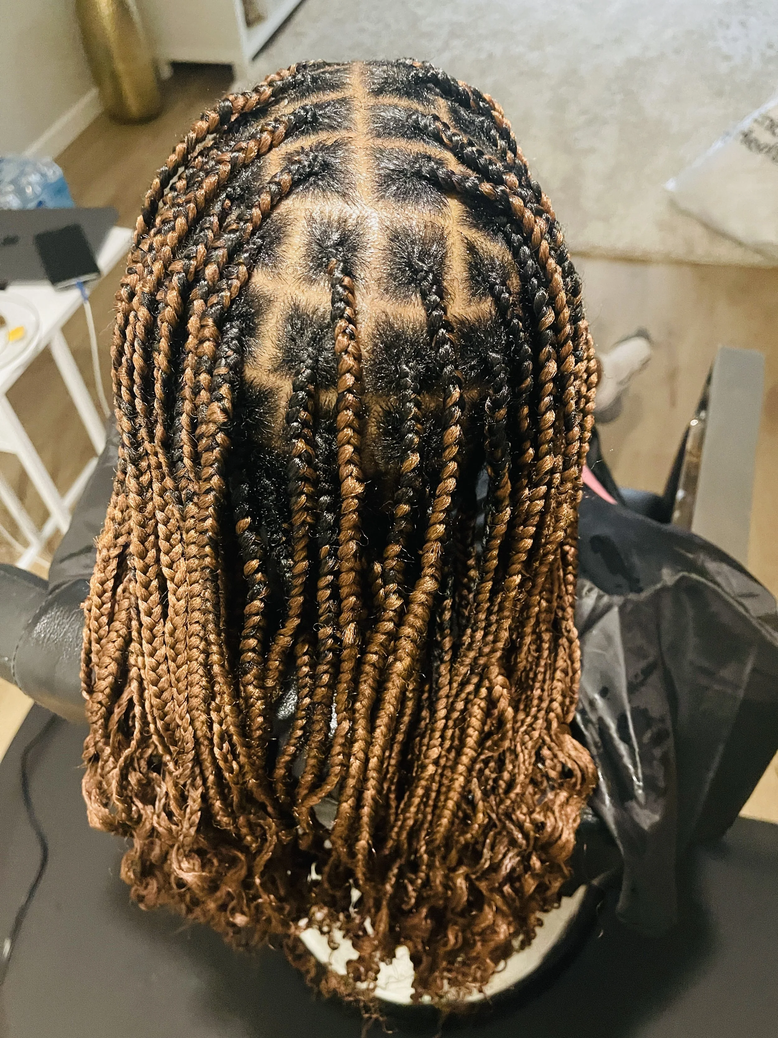 Top view of a person's head with long, brown and black braided hair, sitting in a salon chair.