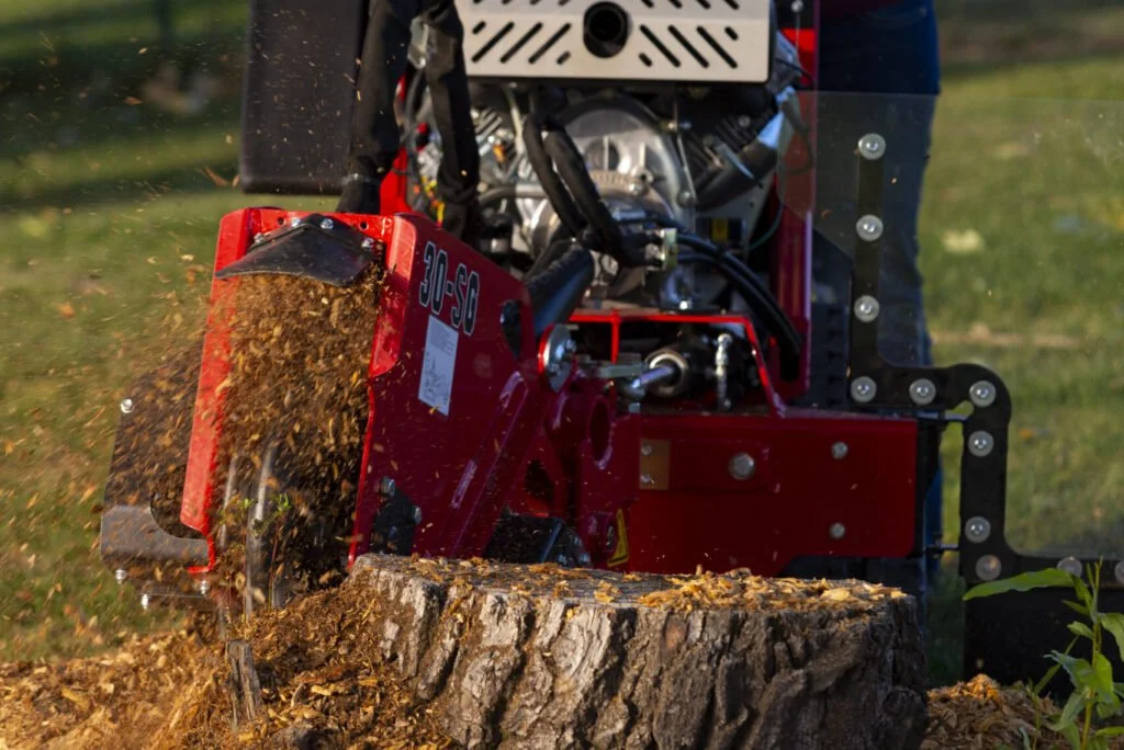 A red forestry mulcher cutting a fallen tree trunk on grass.