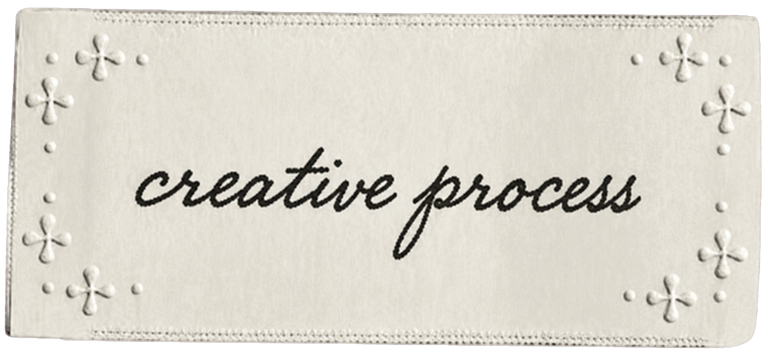 A white fabric piece with embroidered flower patterns in the corners, and the words 'creative process' written in black cursive font in the center.