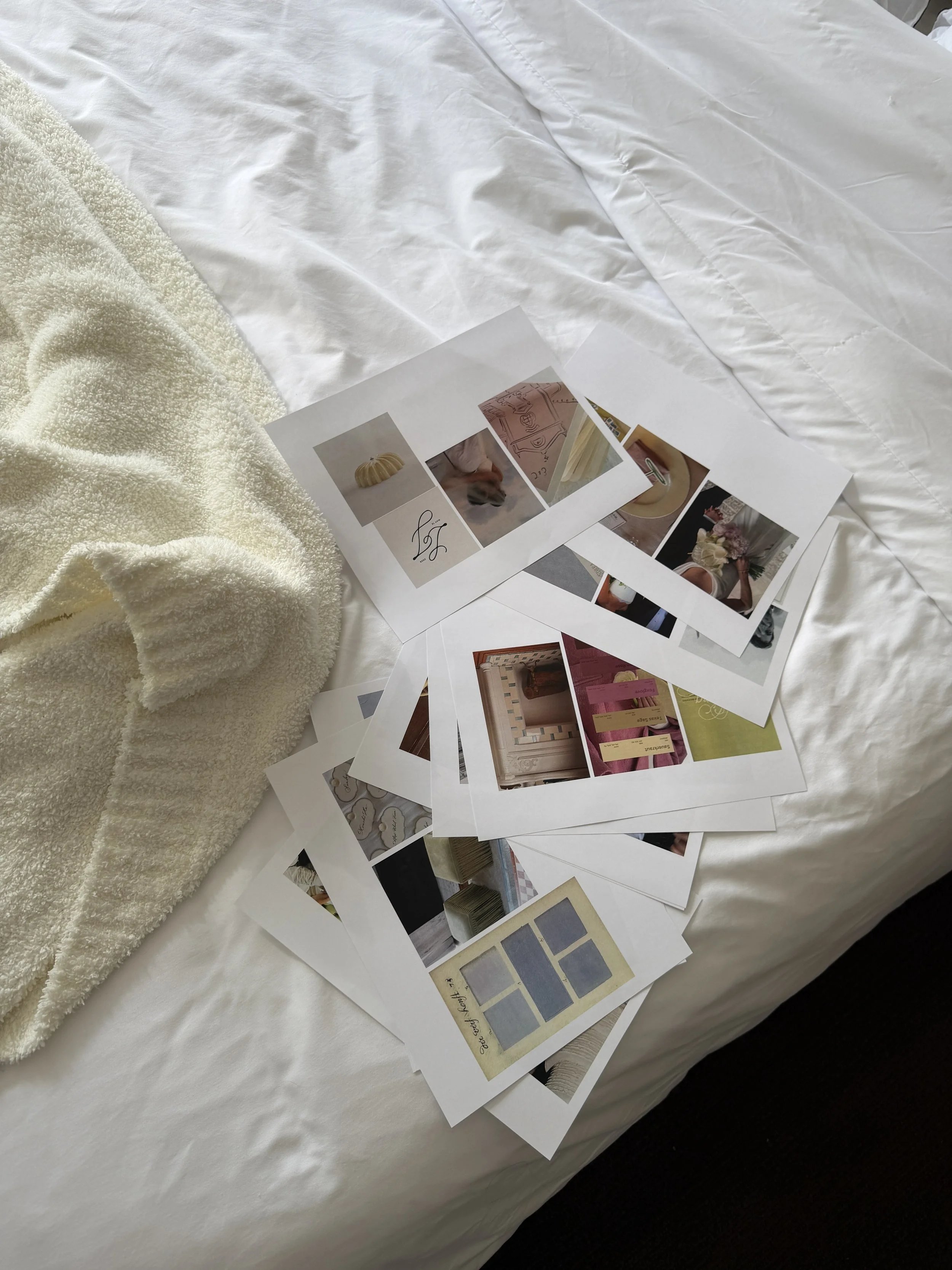 A bed with white sheets, a cream-colored fluffy blanket, and scattered sheets of paper with images and swatches on top.