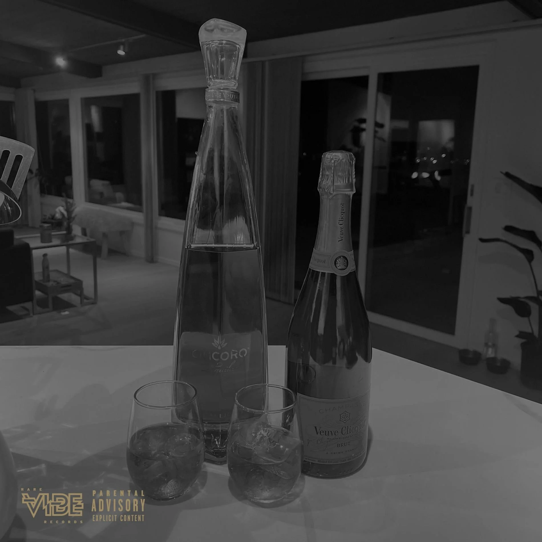 A bottle of Veuve Clicquot champagne and a tall carafe with water, along with two glasses filled with water, on a table in a modern living room at night.