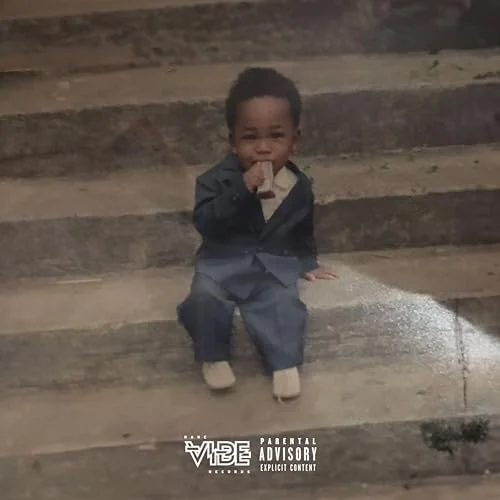 A young child in a dark suit sitting on wooden stairs, drinking from a box.