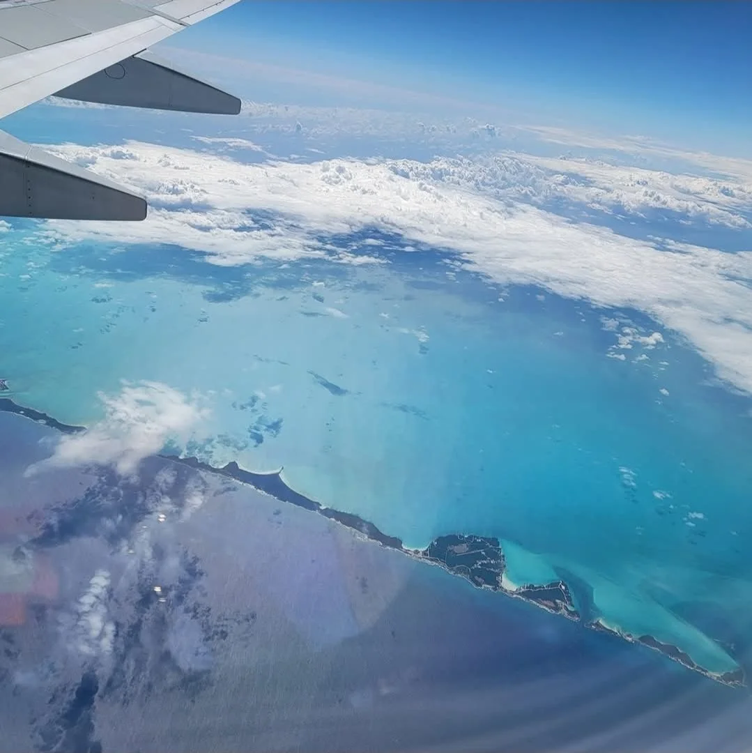 Aerial view of a blue ocean and a coastline from airplane window, with part of the aircraft wing visible.