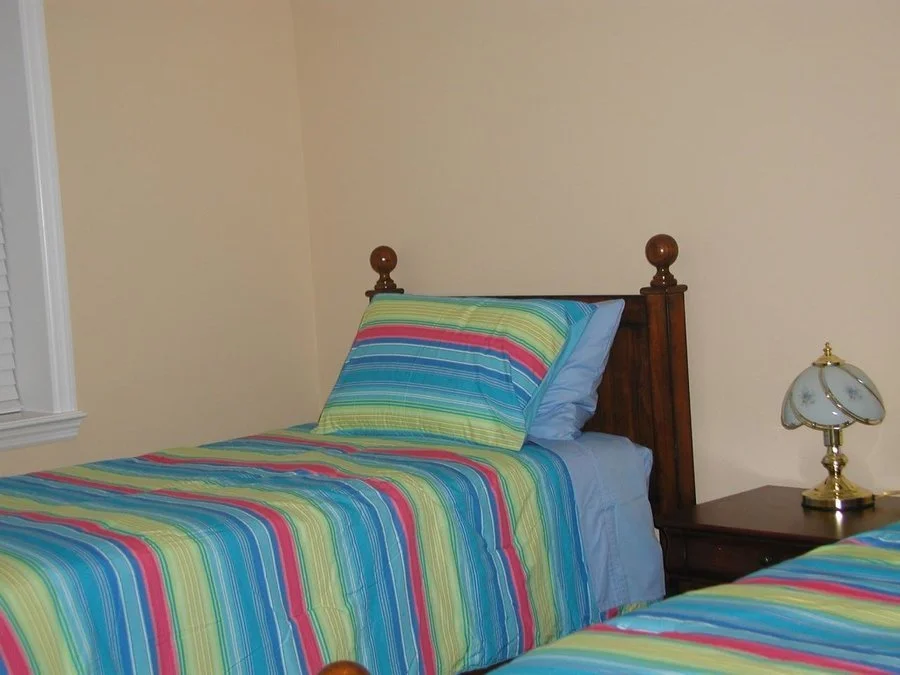 A bedroom with two twin beds with colorful striped bedding, a wooden headboard, and a bedside table with a vintage lamp.