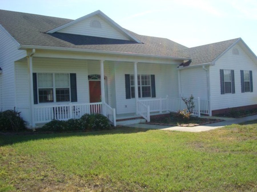 Front view of a white house with a porch, black shutters, and a small lawn.