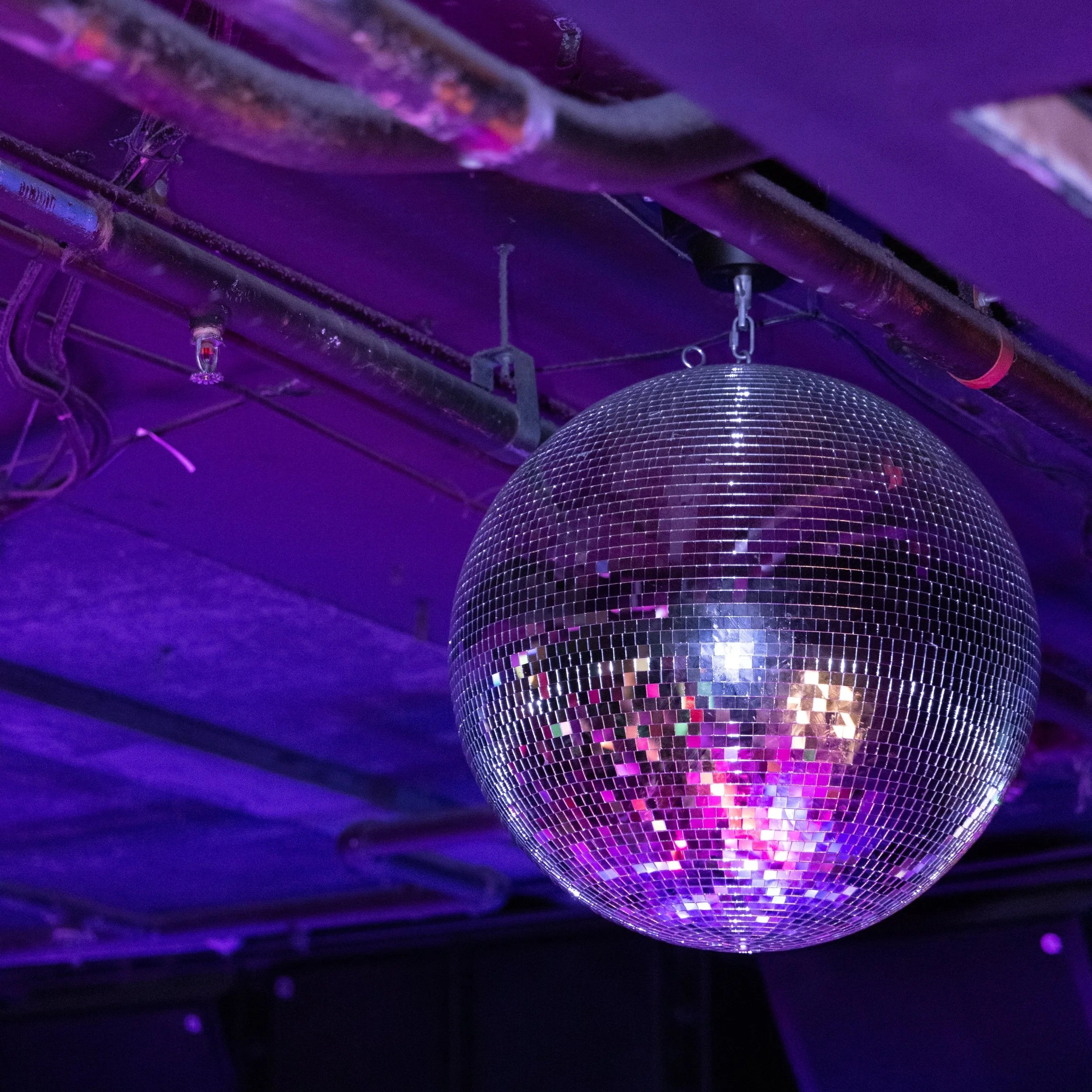 A disco ball hanging from the ceiling with purple lighting in the background.