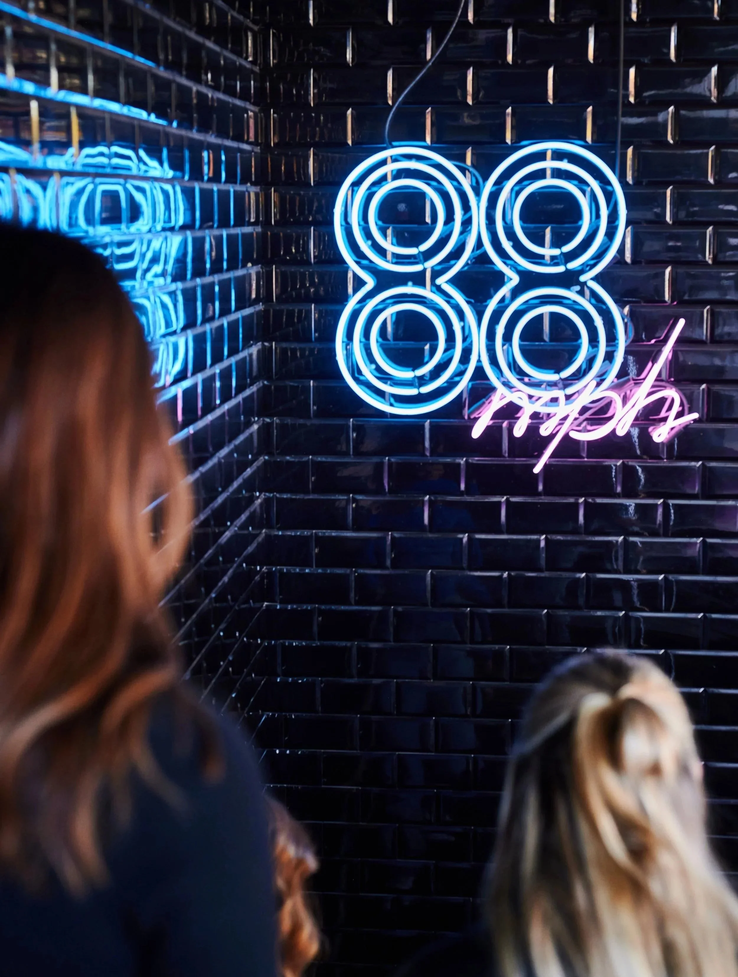 Neon sign on a dark glossy wall displaying the number 84 in blue and pink colors.