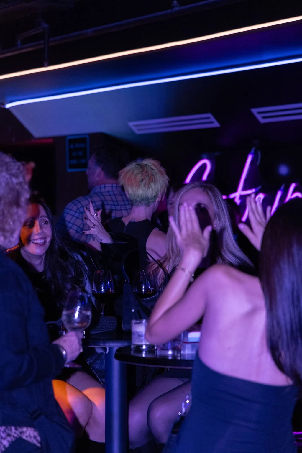 Group of people socializing and having fun at a nightclub or bar with purple and blue neon lighting.