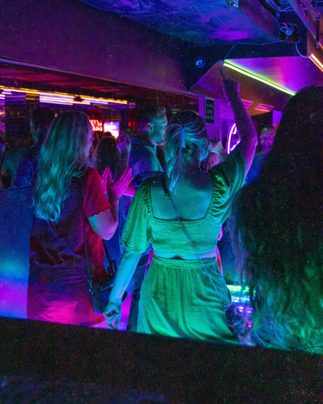 People dancing and socializing in a dark, colorful nightclub with neon lights.