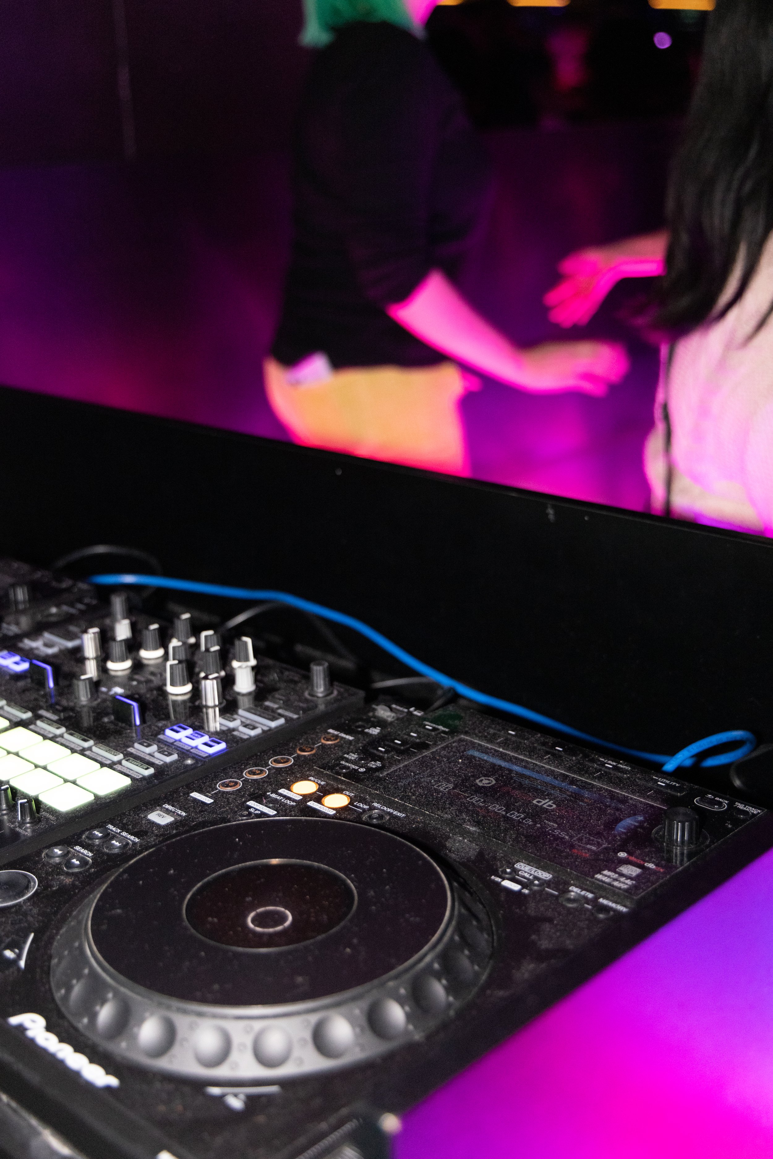 DJ equipment with a Pioneer DJ controller and a dark background with purple and pink lights.
