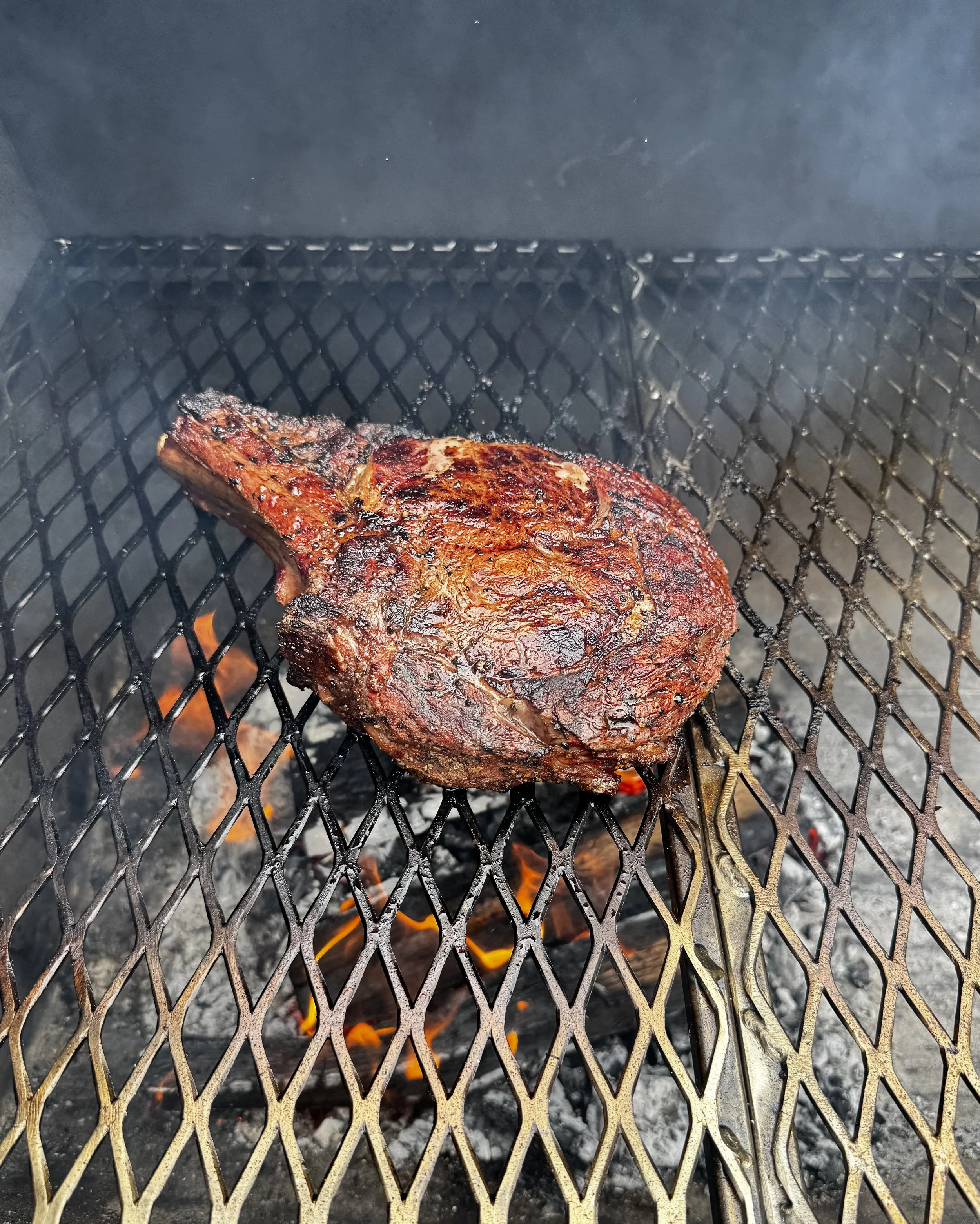 A grilled beef steak with a charred surface cooking inside a barbecue grill.