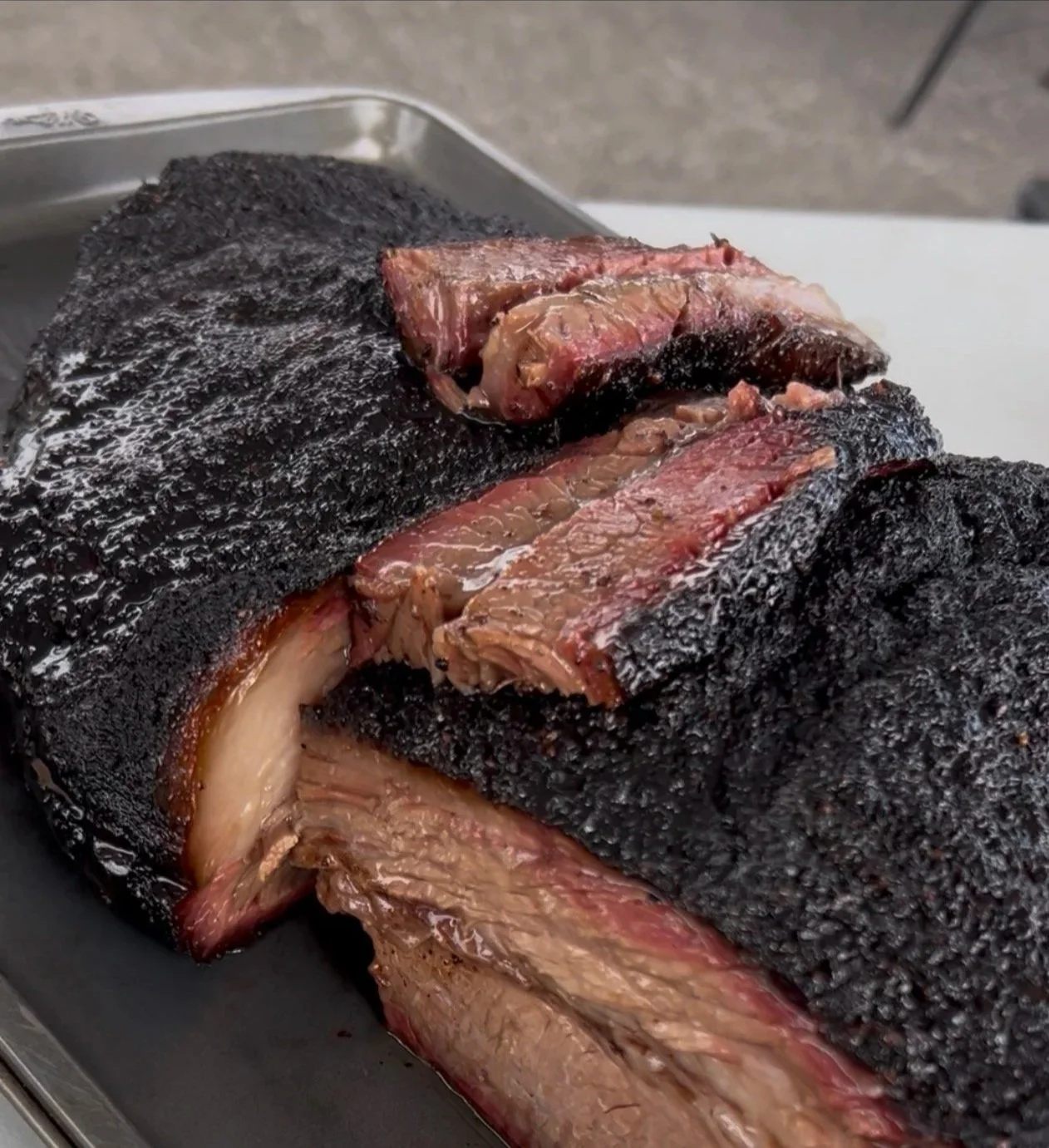 A large smoked brisket with a dark bark, partially sliced to show tender, juicy meat inside.