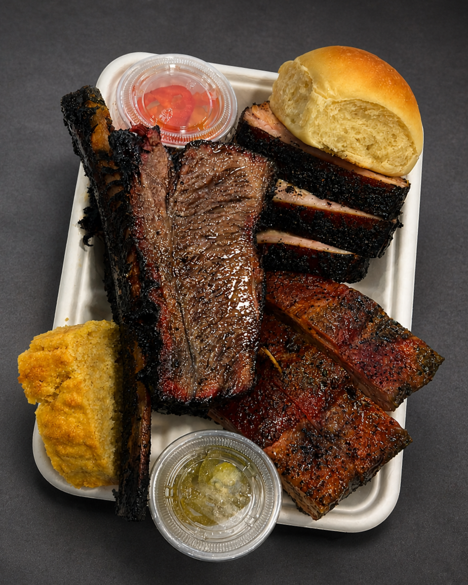 Assorted barbecue meats with two slices of bread and two small containers of sauce, one with honey mustard and the other with barbecue sauce, on a white serving tray.
