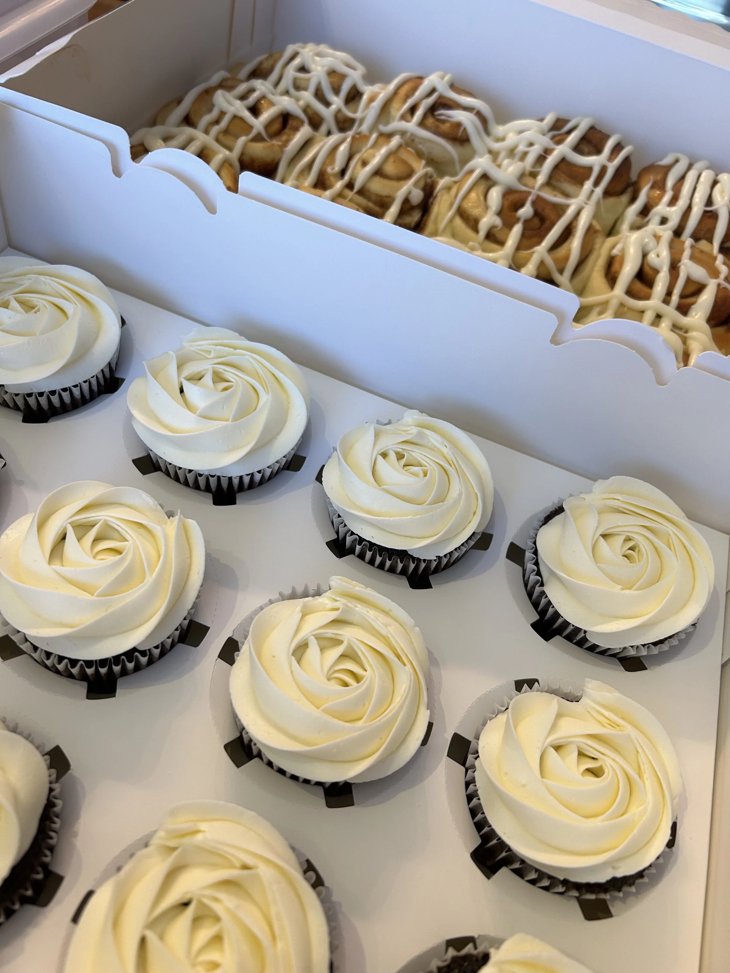 Tray of vanilla cupcakes with white swirl frosting and a tray of cinnamon rolls with icing.