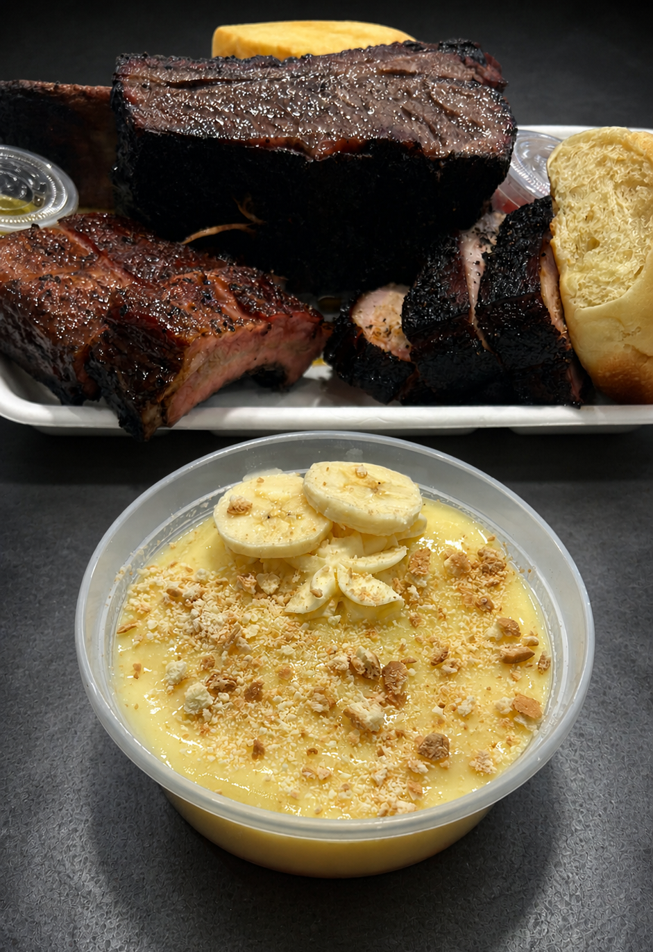 Barbecue ribs, brisket, and baked potato on a platter, with a bowl of banana pudding topped with banana slices and crumbled cookies in the foreground.