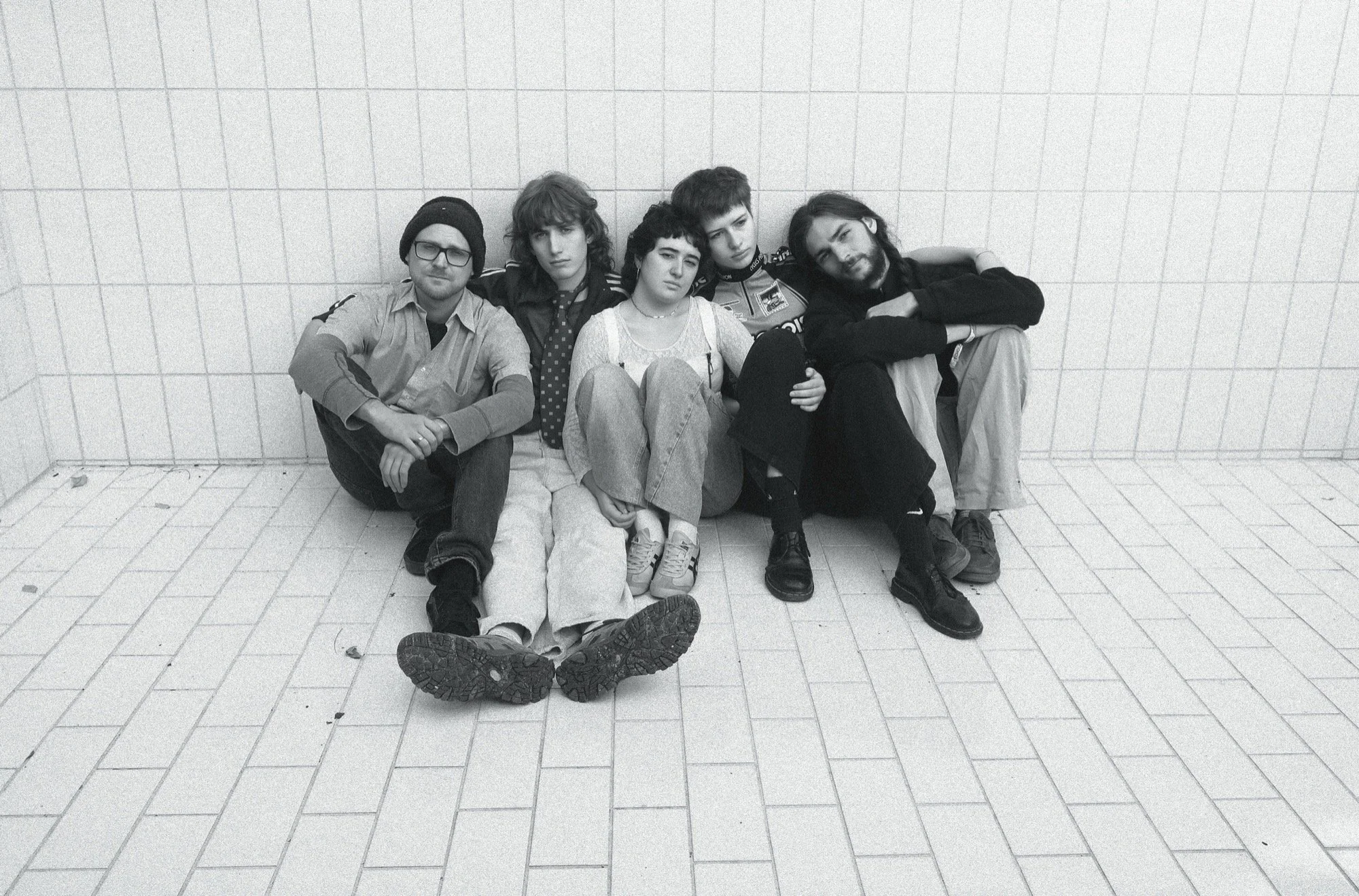 Via Fucina members including Camille Santacroce sitting against a tiled wall, in casual clothing, black and white photo.