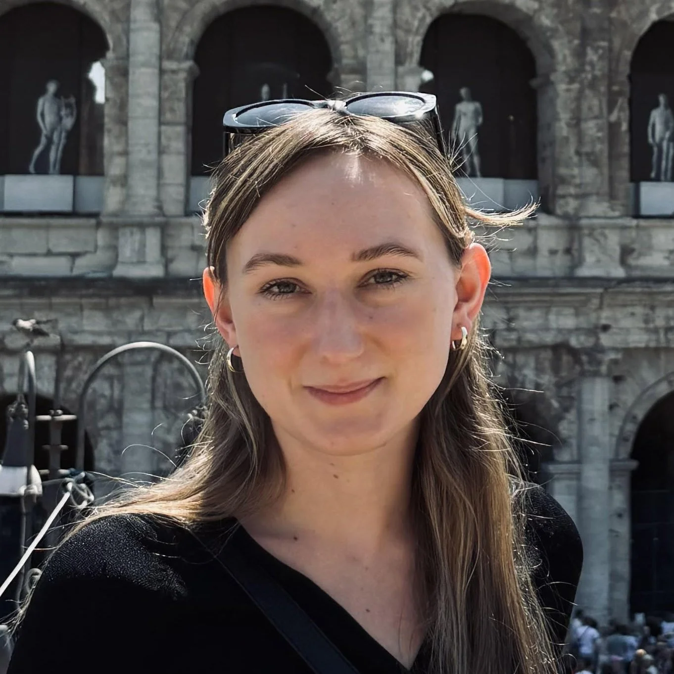 Young woman with glasses on her head, smiling outdoors in front of historic stone architecture with statues.