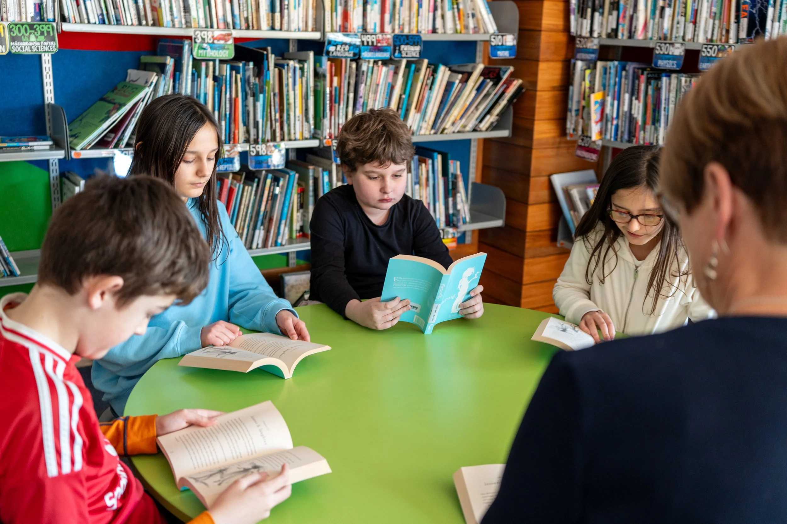 Children reading books around a green table in a library.