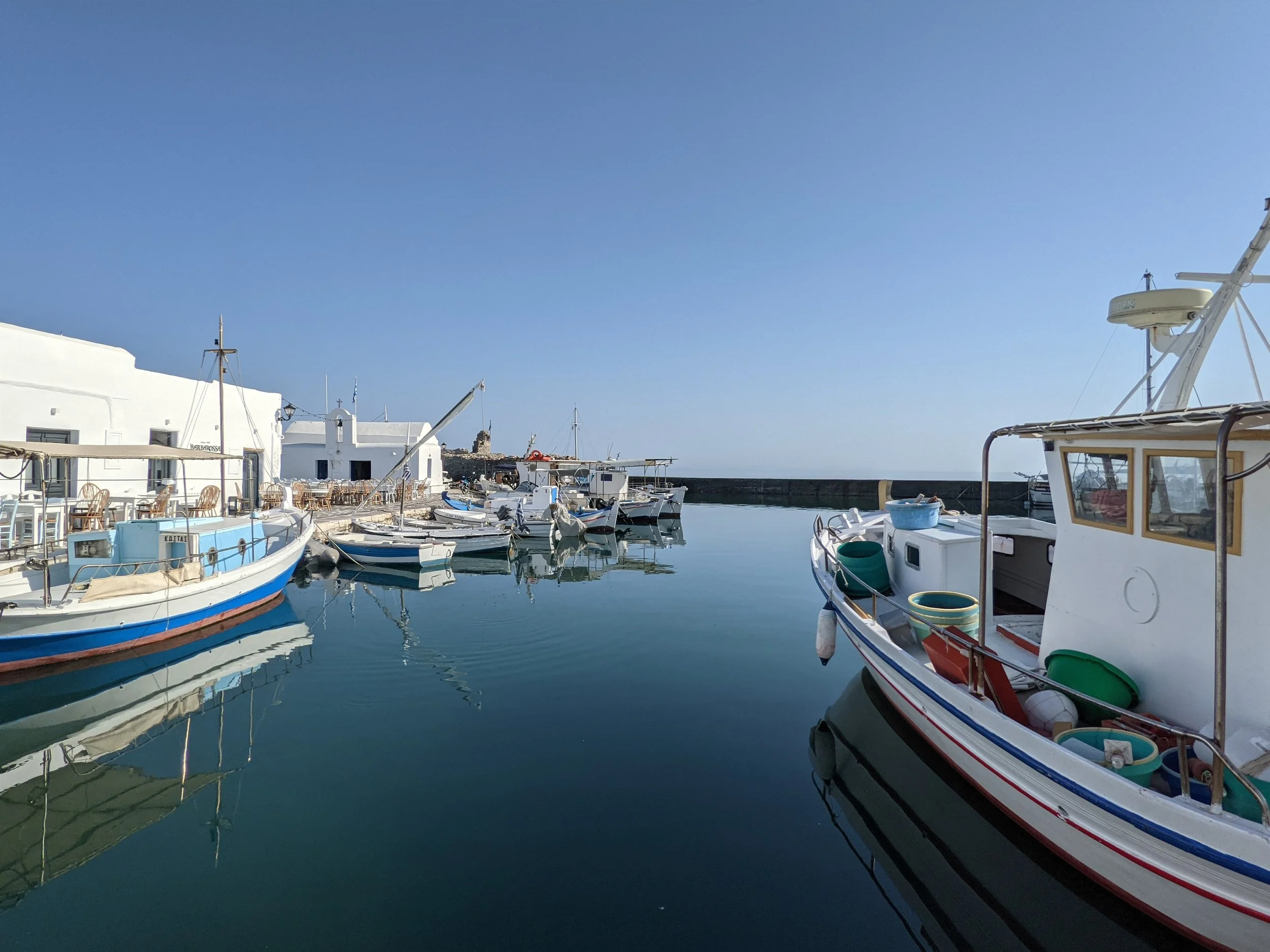 Boats docked in a marina with white buildings and a clear blue sky in the background.