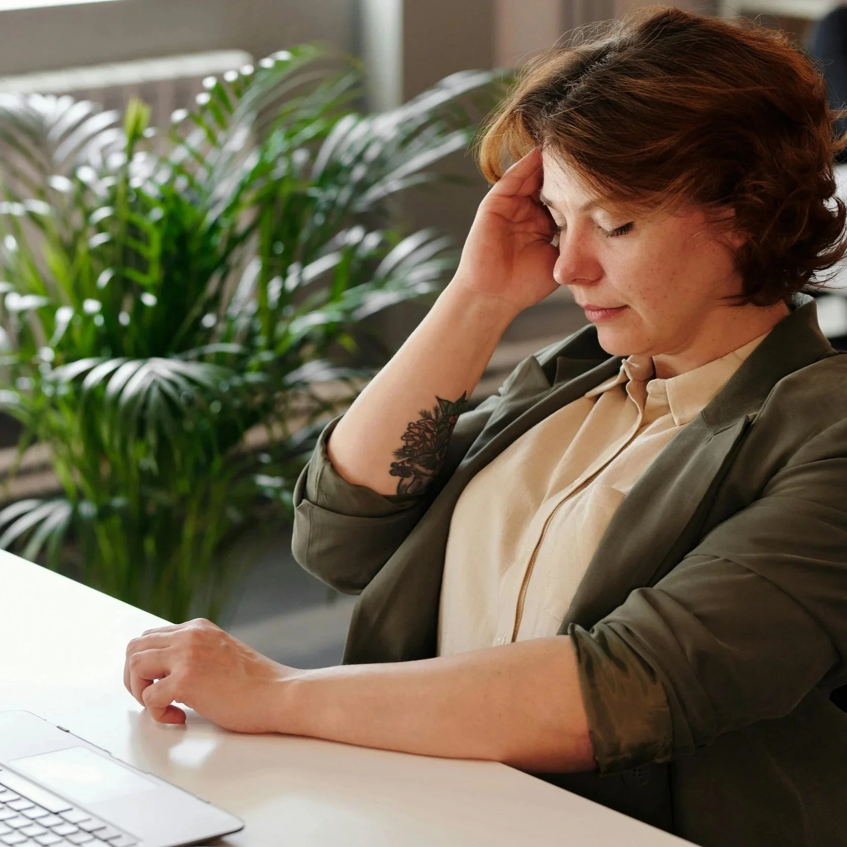 Professional woman experiencing workplace anxiety and stress while working at a laptop in an office setting