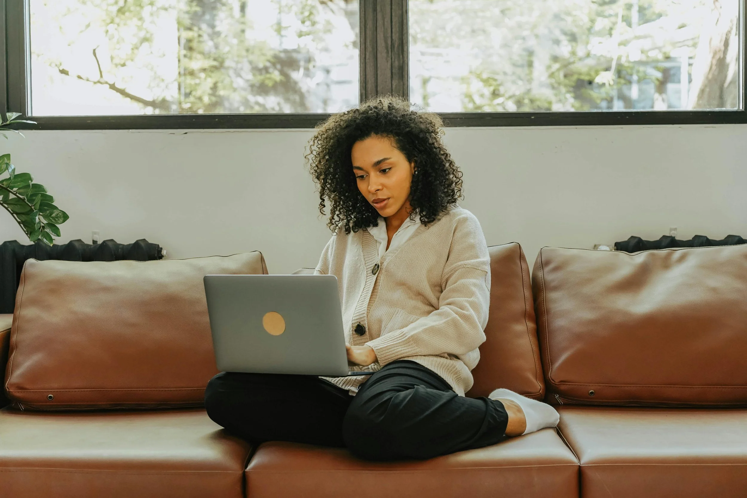 Woman sitting on a couch with a laptop attending an online therapy session for imposter syndrome from home
