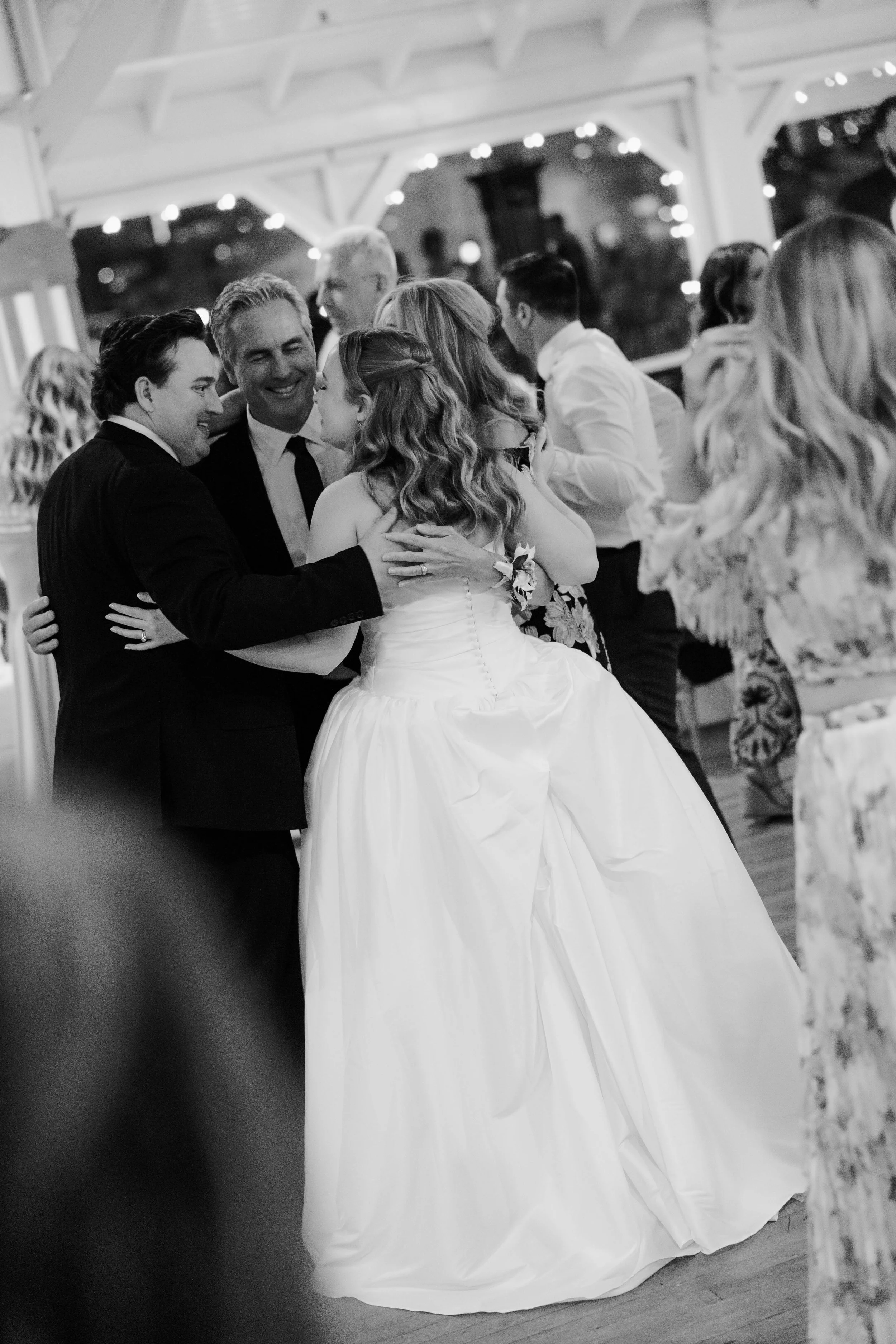 Black and white photo of a wedding reception showing a bride and groom dancing with family and friends.
