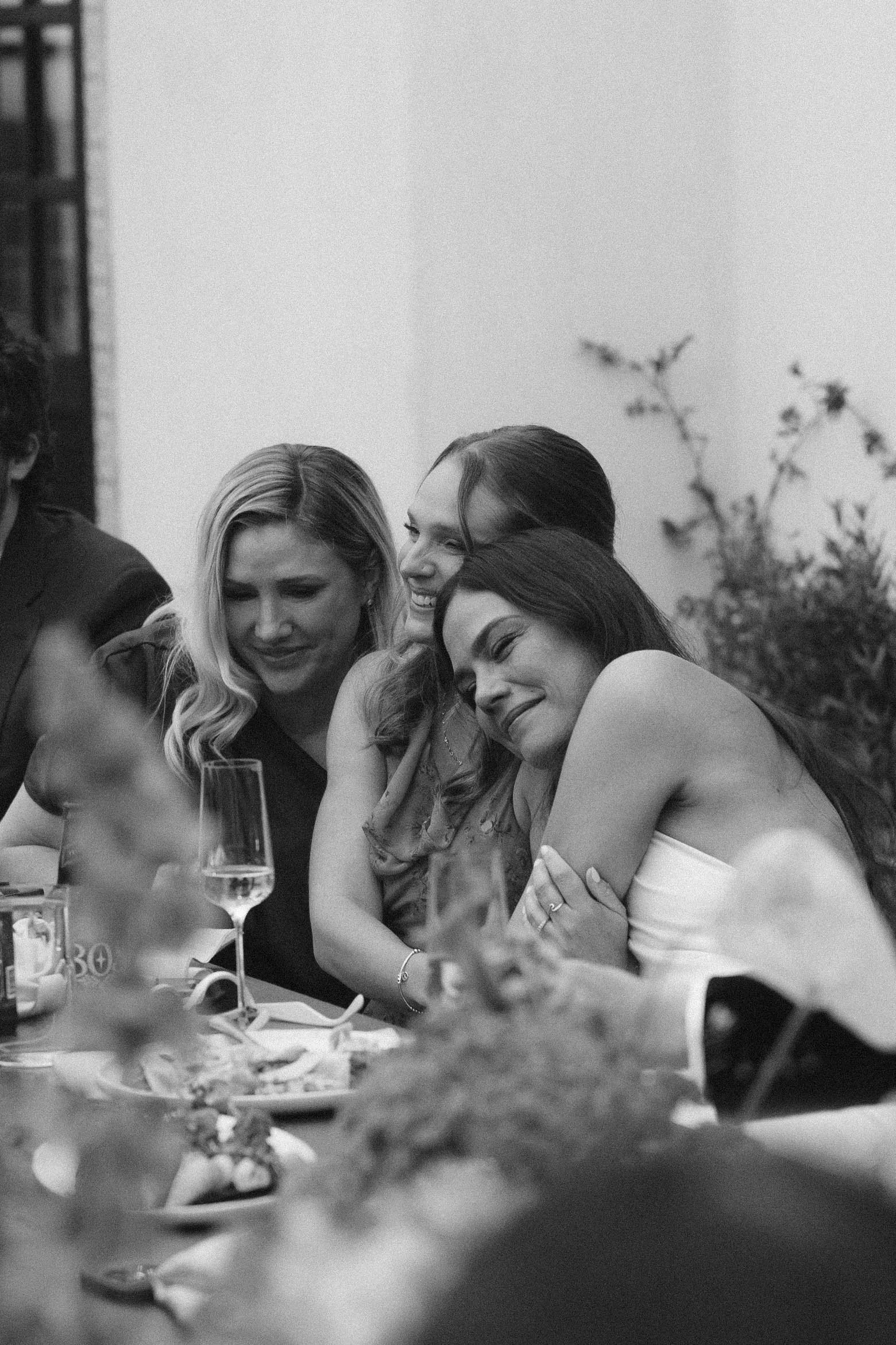 A group of women is sitting together at a table at a social gathering, smiling and enjoying each other's company.