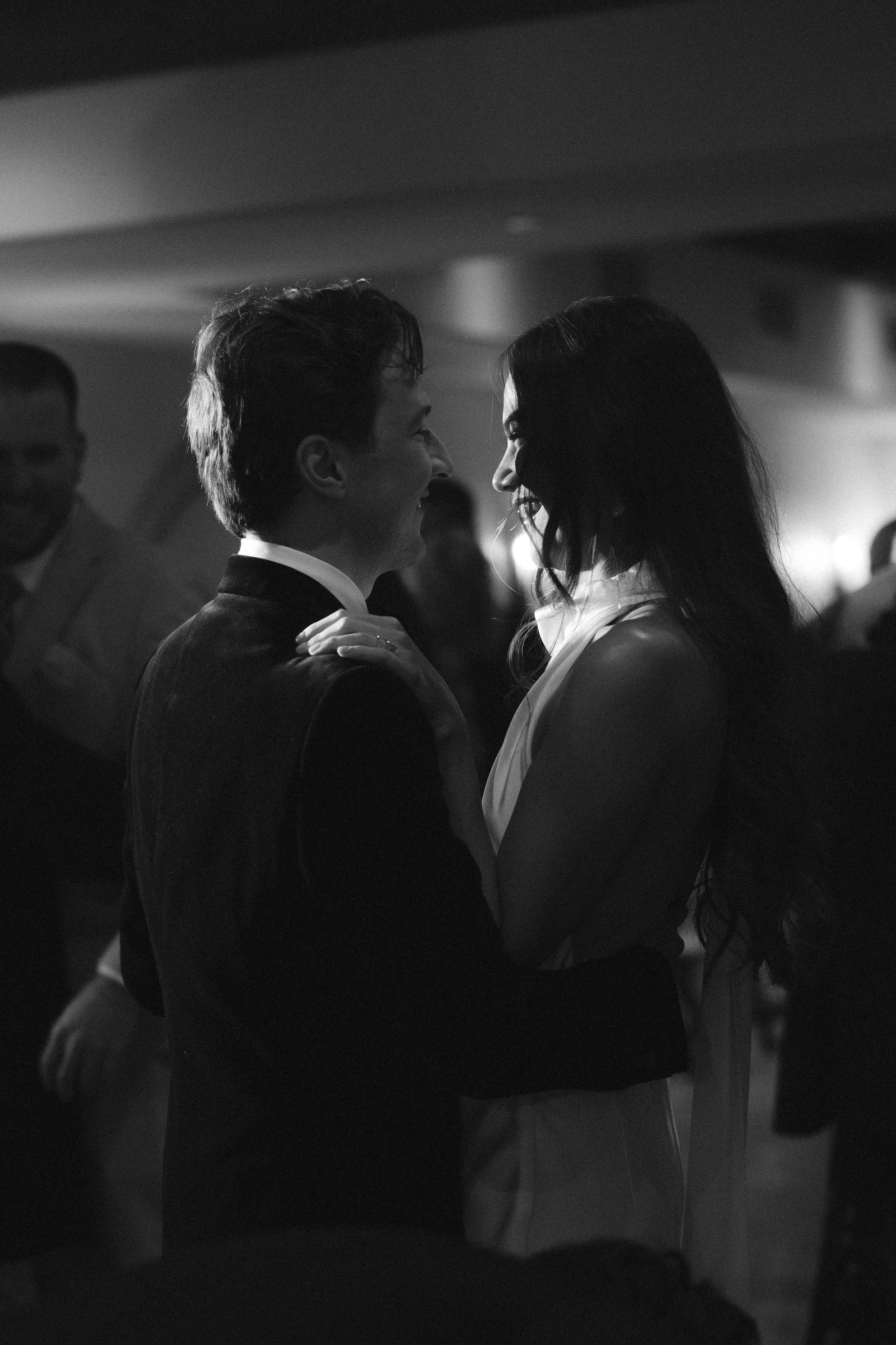 A black-and-white photograph of a couple dancing closely together at a formal event, with other people visible in the background.