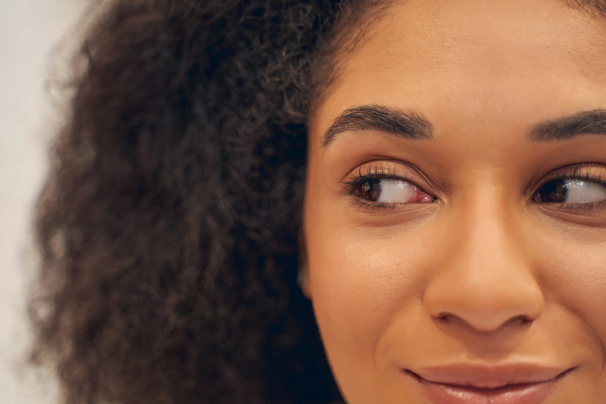A close-up of a smiling woman with curly dark hair, brown eyes, and smooth skin.
