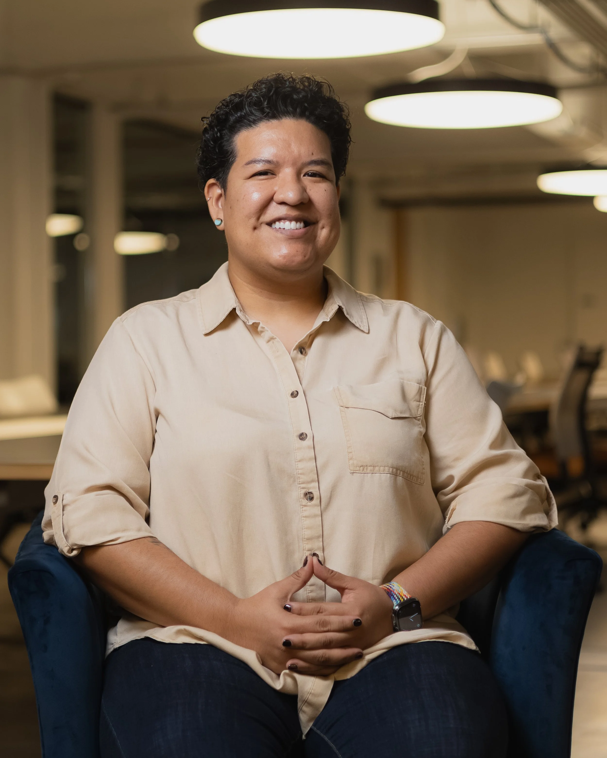 Woman smiling and sitting in a blue armchair in an office environment.