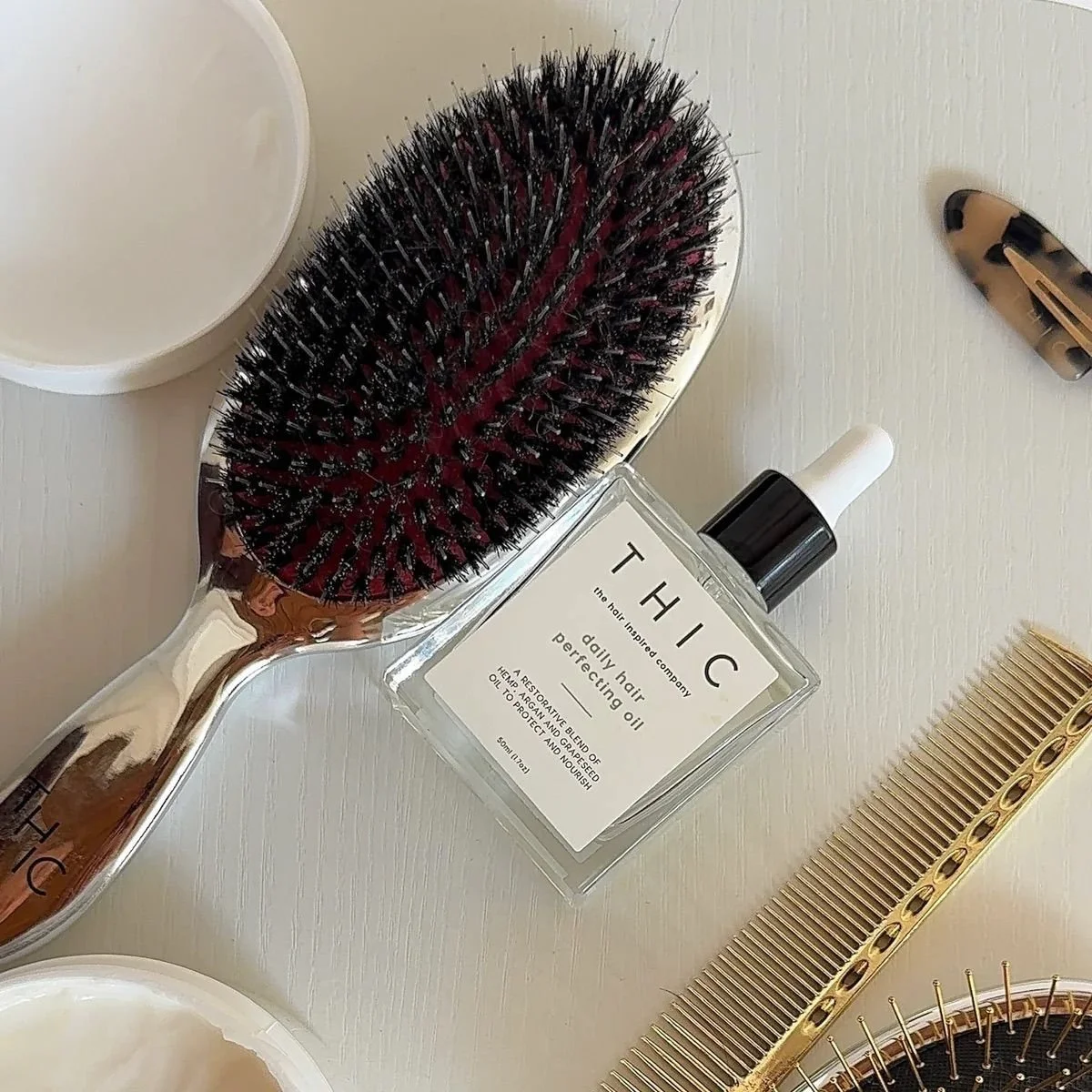 Hairbrush, hair oil, hair comb, and hair clips on a white surface.