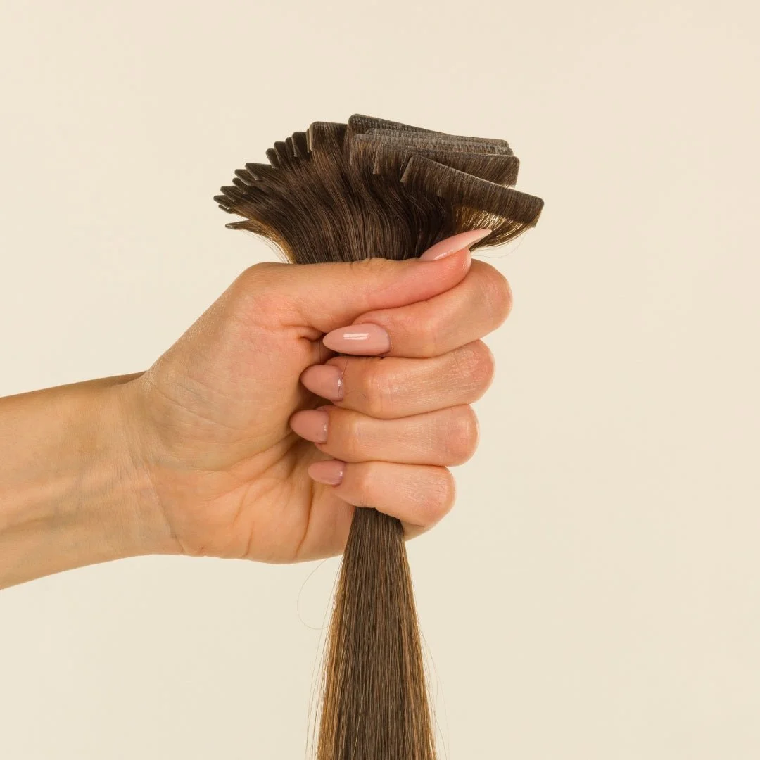 A hand holding a sample of hair extensions or weaves, with the hair being light brown.